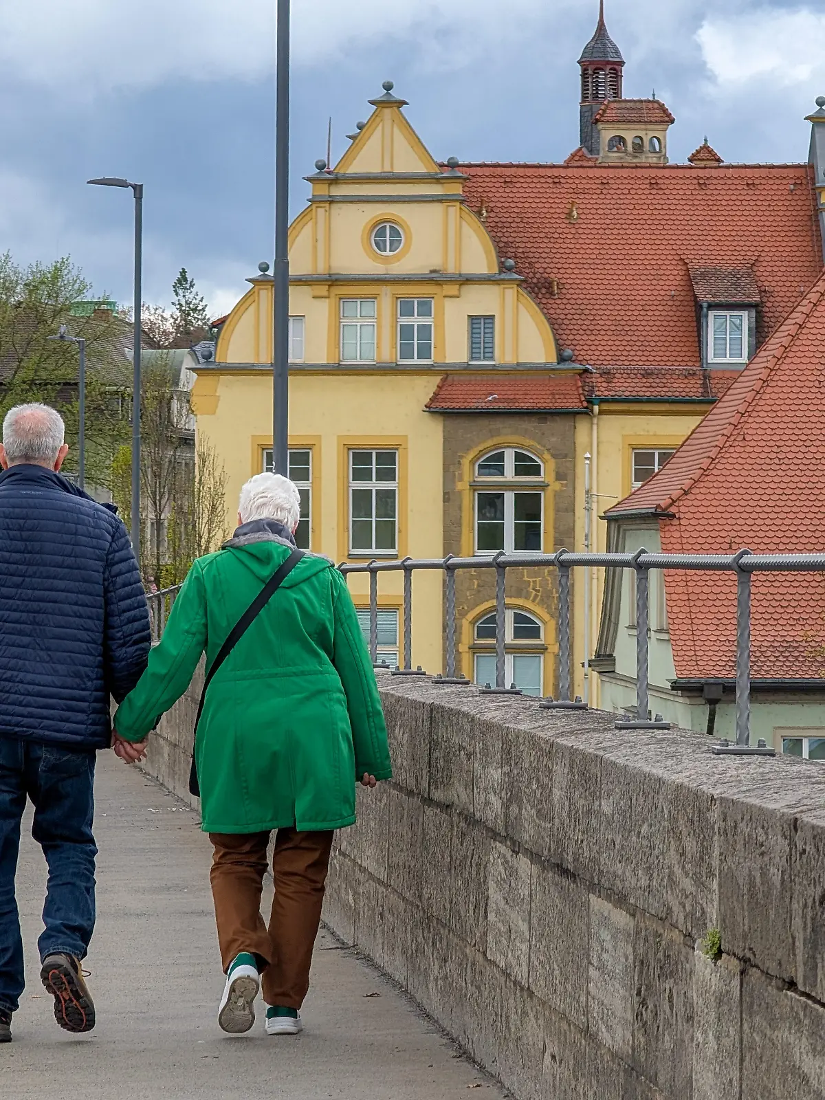 A senior couple walks hand in hand on a bridge in Kitzingen, Lower Franconia, Bavaria, Germany, on April 19, 2026. The presence of older residents in public spaces highlights the role of demographic aging, retirement, and pension security in Germany's social and economic planning. (Photo by Michael Nguyen/NurPhoto)