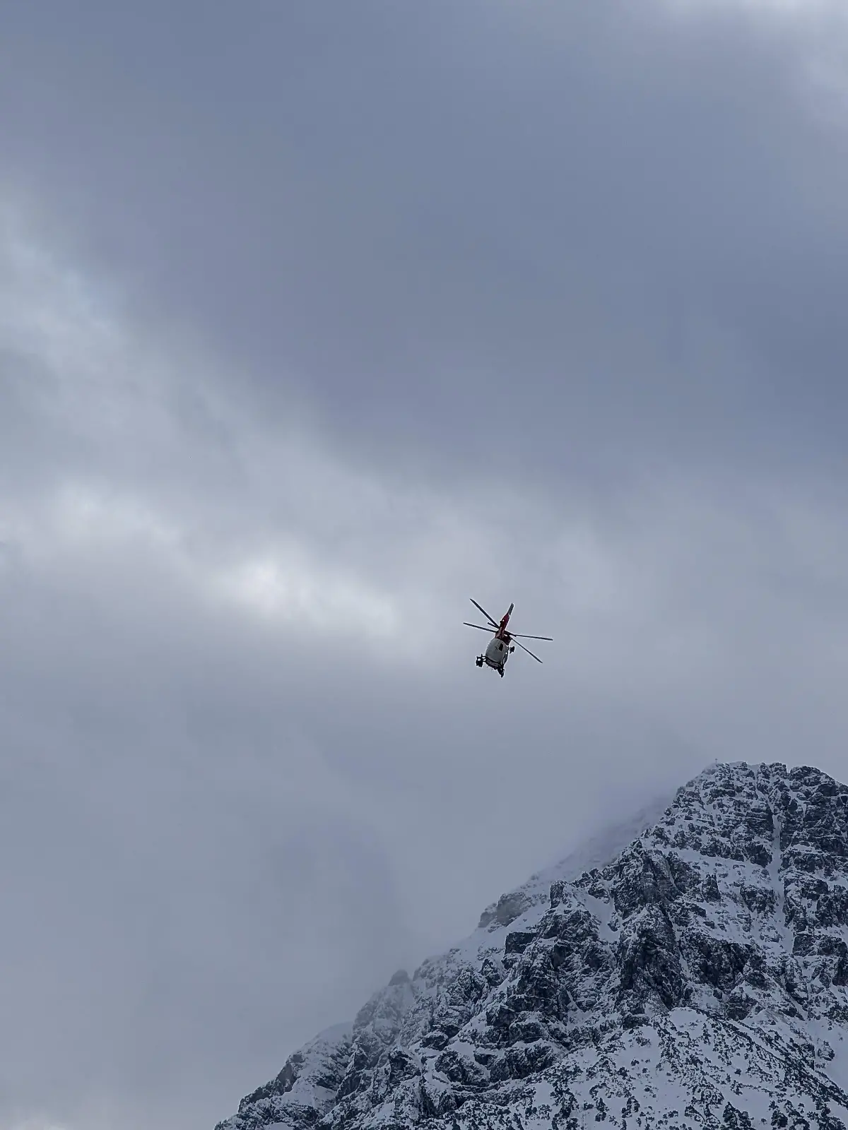 A mountain emergency rescue helicopter flies over a snow-covered mountain peak in Reutte, Tyrol, Austria, on January 3, 2026. The state-of-the-art red and white aircraft is utilized for challenging search and rescue missions in the alpine terrain of the greater Reutte area. (Photo by Michael Nguyen/NurPhoto)