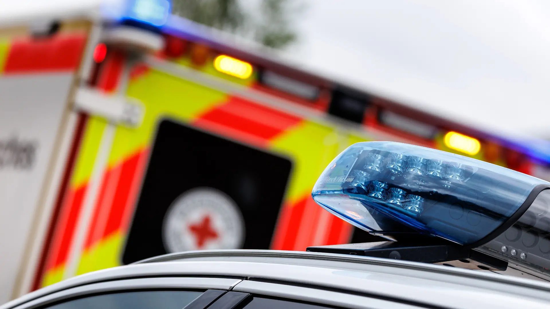 Das eingeschaltete Blaulicht ist bei einem Rettungseinsatz auf einem Rettungswagen vom Bayerischen Roten Kreuz in Schäftlarn (Bayern) zu sehen. Im Vordergrund ist das Blaulicht auf einem Einsatzfahrzeug der Polizei zu sehen.