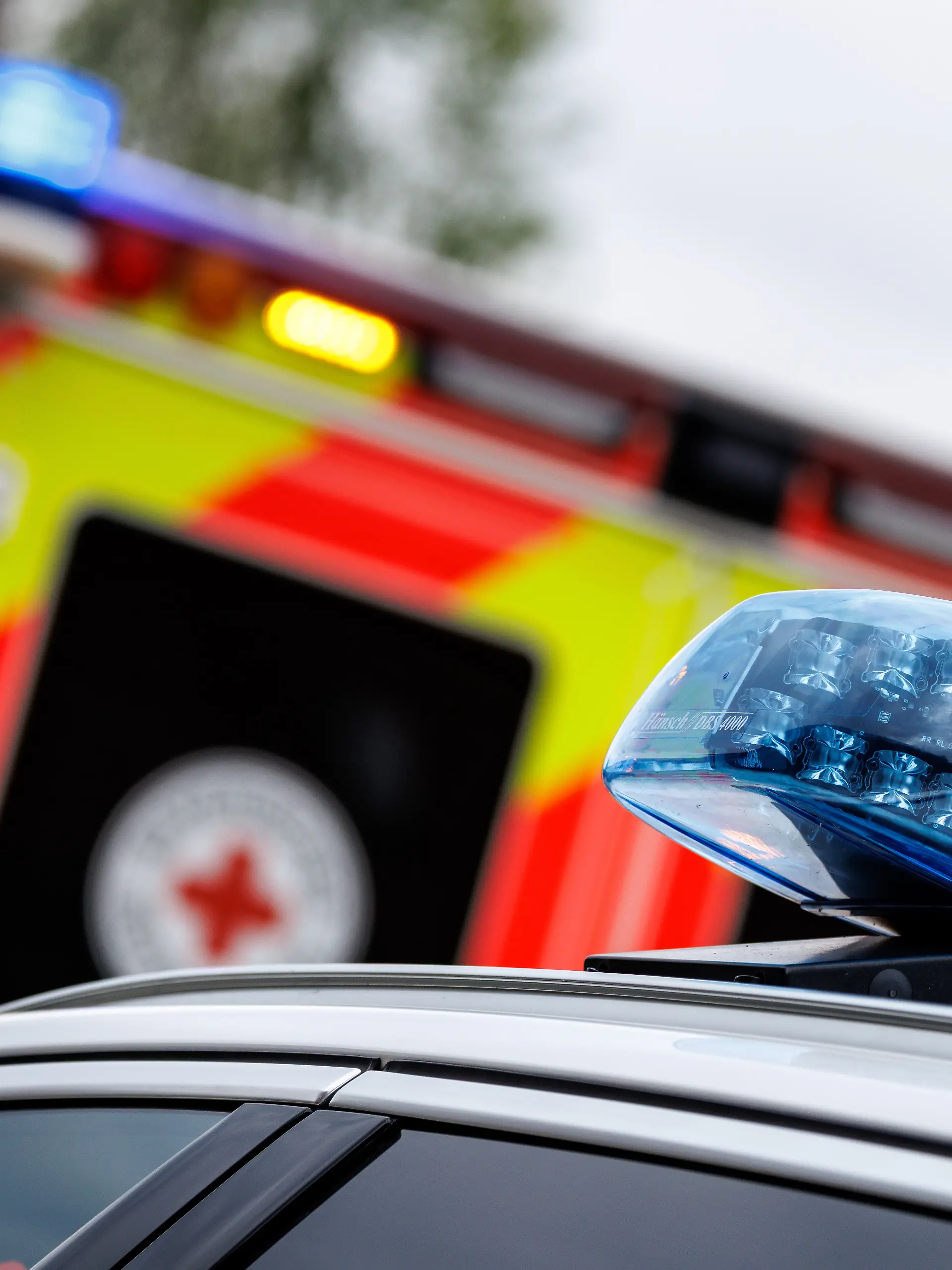 Das eingeschaltete Blaulicht ist bei einem Rettungseinsatz auf einem Rettungswagen vom Bayerischen Roten Kreuz in Schäftlarn (Bayern) zu sehen. Im Vordergrund ist das Blaulicht auf einem Einsatzfahrzeug der Polizei zu sehen.