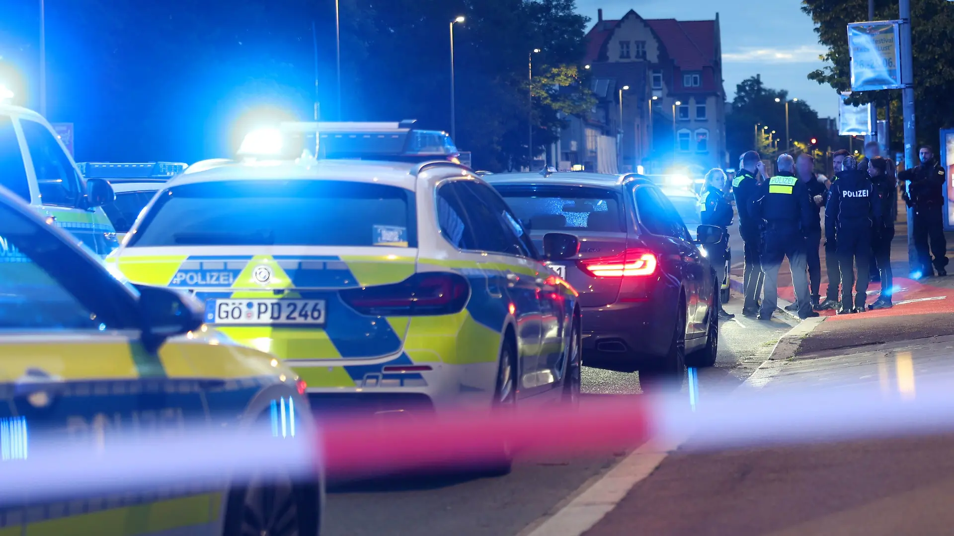 13.06.2026, Niedersachsen, Göttingen: Polizisten und Polizeifahrzeuge stehen hinter einer Absperrung. Ein Polizist ist bei einer Auseinandersetzung zwischen zwei Personengruppen im niedersächsischen Göttingen angeschossen worden. Der Beamte sei ins Krankenhaus gebracht worden, wo er derzeit behandelt werde, teilte die Polizei mit. Zur Schwere der Verletzungen machte sie zunächst keine Angaben. Foto: Stefan Rampfel/dpa - ACHTUNG: Person(en) wurde(n) aus rechtlichen Gründen gepixelt +++ dpa-Bildfunk +++