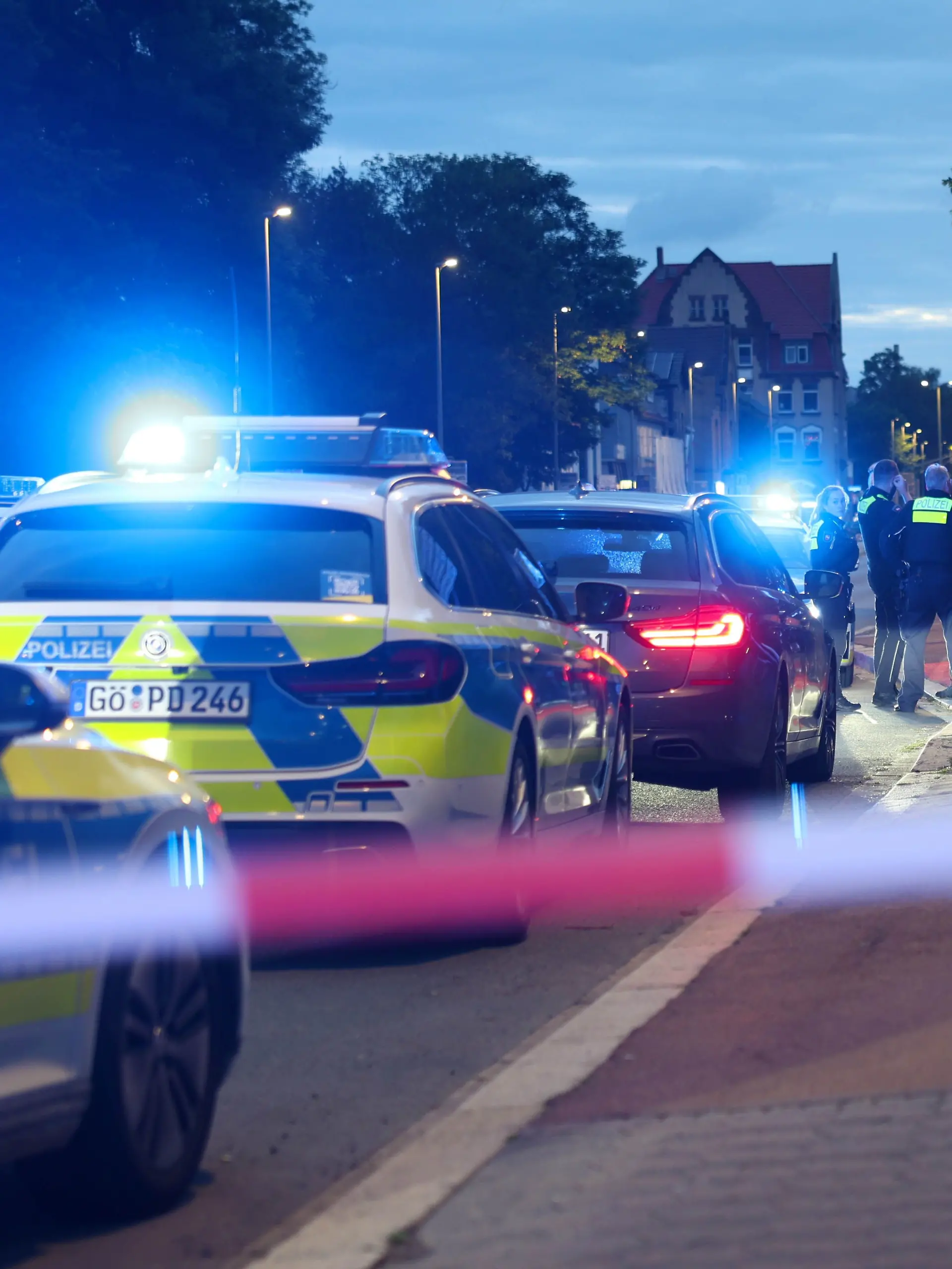 13.06.2026, Niedersachsen, Göttingen: Polizisten und Polizeifahrzeuge stehen hinter einer Absperrung. Ein Polizist ist bei einer Auseinandersetzung zwischen zwei Personengruppen im niedersächsischen Göttingen angeschossen worden. Der Beamte sei ins Krankenhaus gebracht worden, wo er derzeit behandelt werde, teilte die Polizei mit. Zur Schwere der Verletzungen machte sie zunächst keine Angaben. Foto: Stefan Rampfel/dpa - ACHTUNG: Person(en) wurde(n) aus rechtlichen Gründen gepixelt +++ dpa-Bildfunk +++