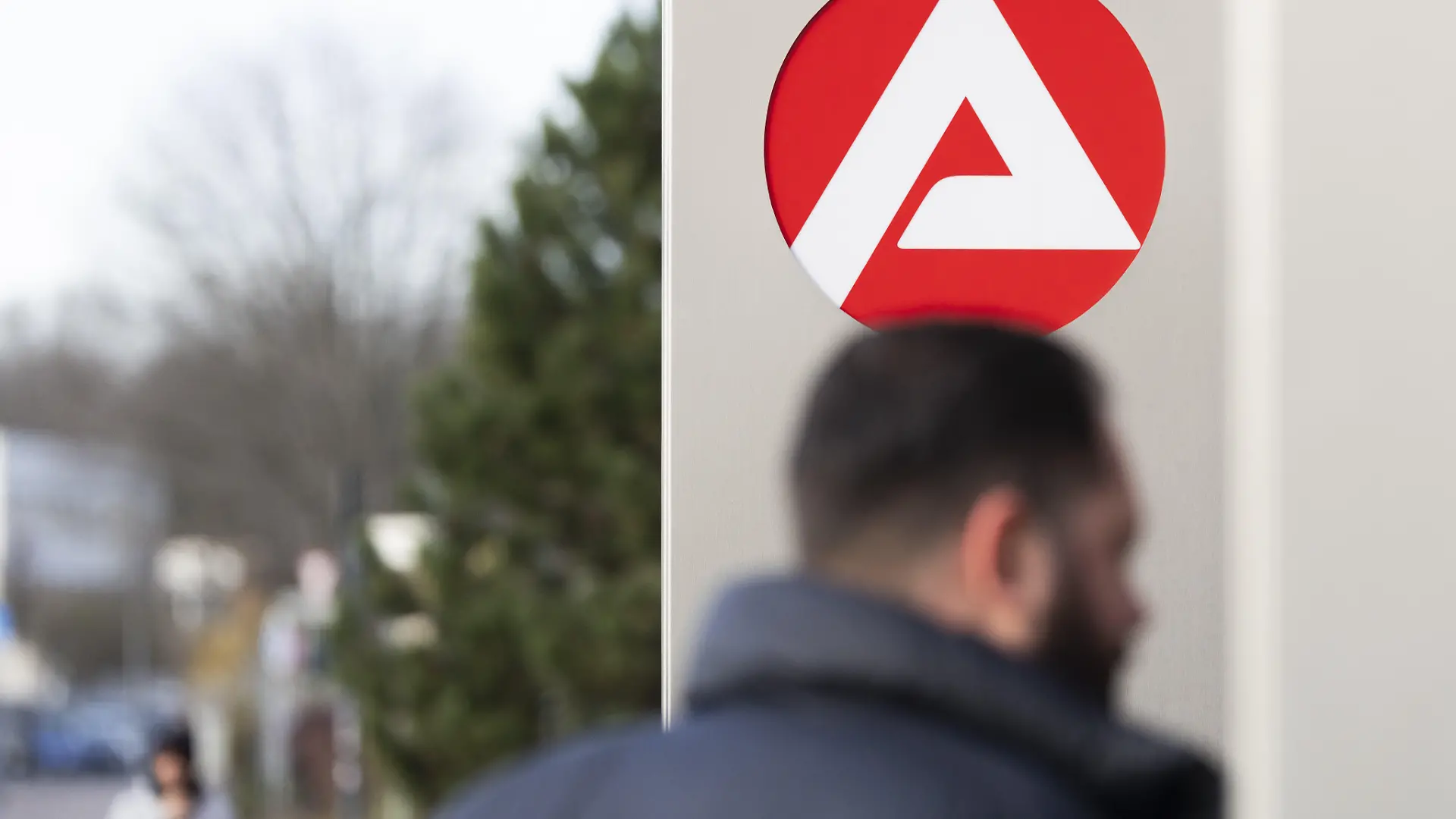 Stele mit dem Zeichen, Logo der Agentur für Arbeit vor dem Gebäude der Agentur für Arbeit, unscharfe Personen auf dem Weg zur Agentur, Köln, Nordrhein-Westfalen, Deutschland