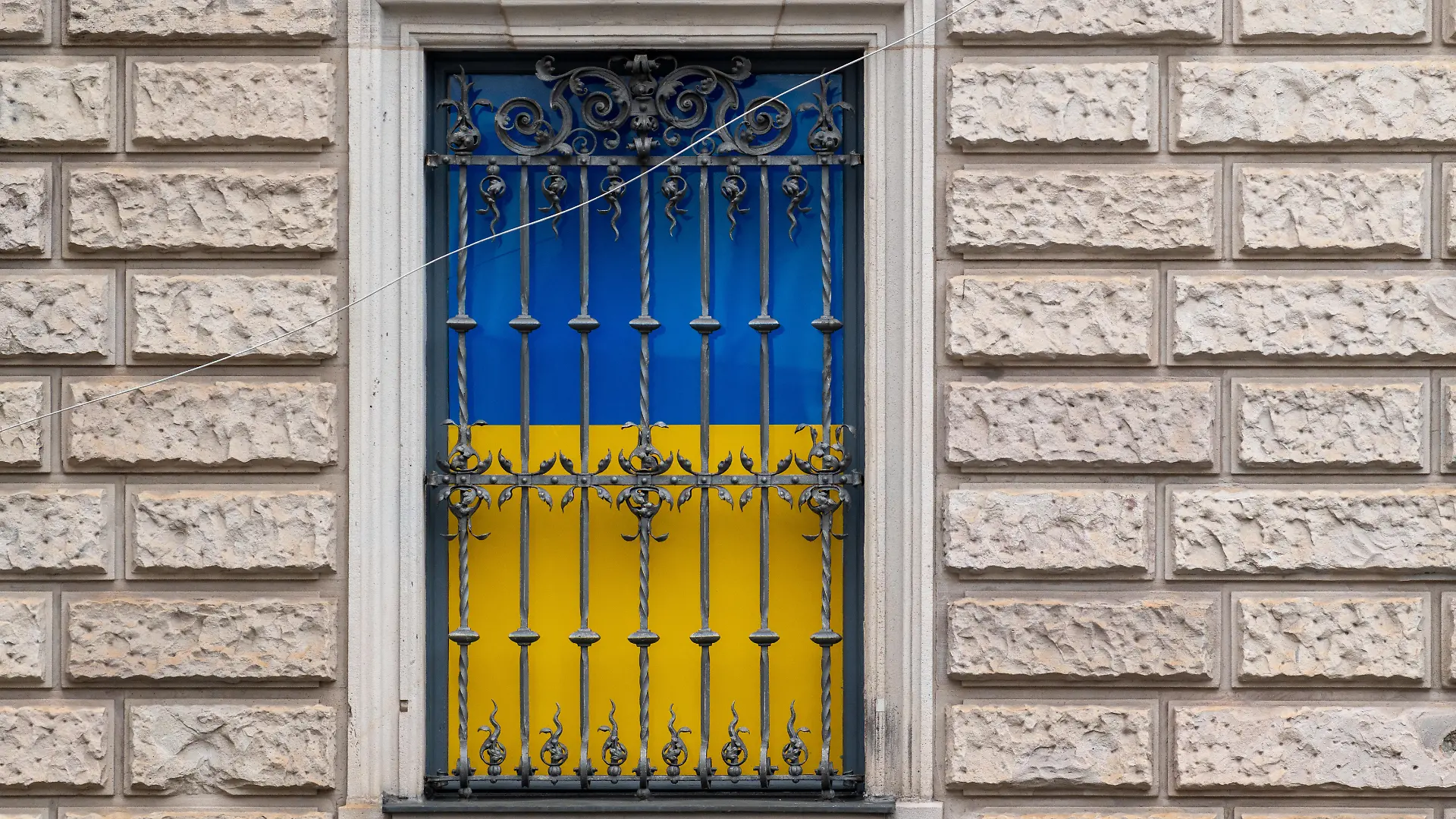 Fenster mit Metallgitter am Ukraine House während der Münchner Sicherheitskonferenz 2026. Hinter dem Gitter sind die Farben der ukrainischen Flagge sichtbar