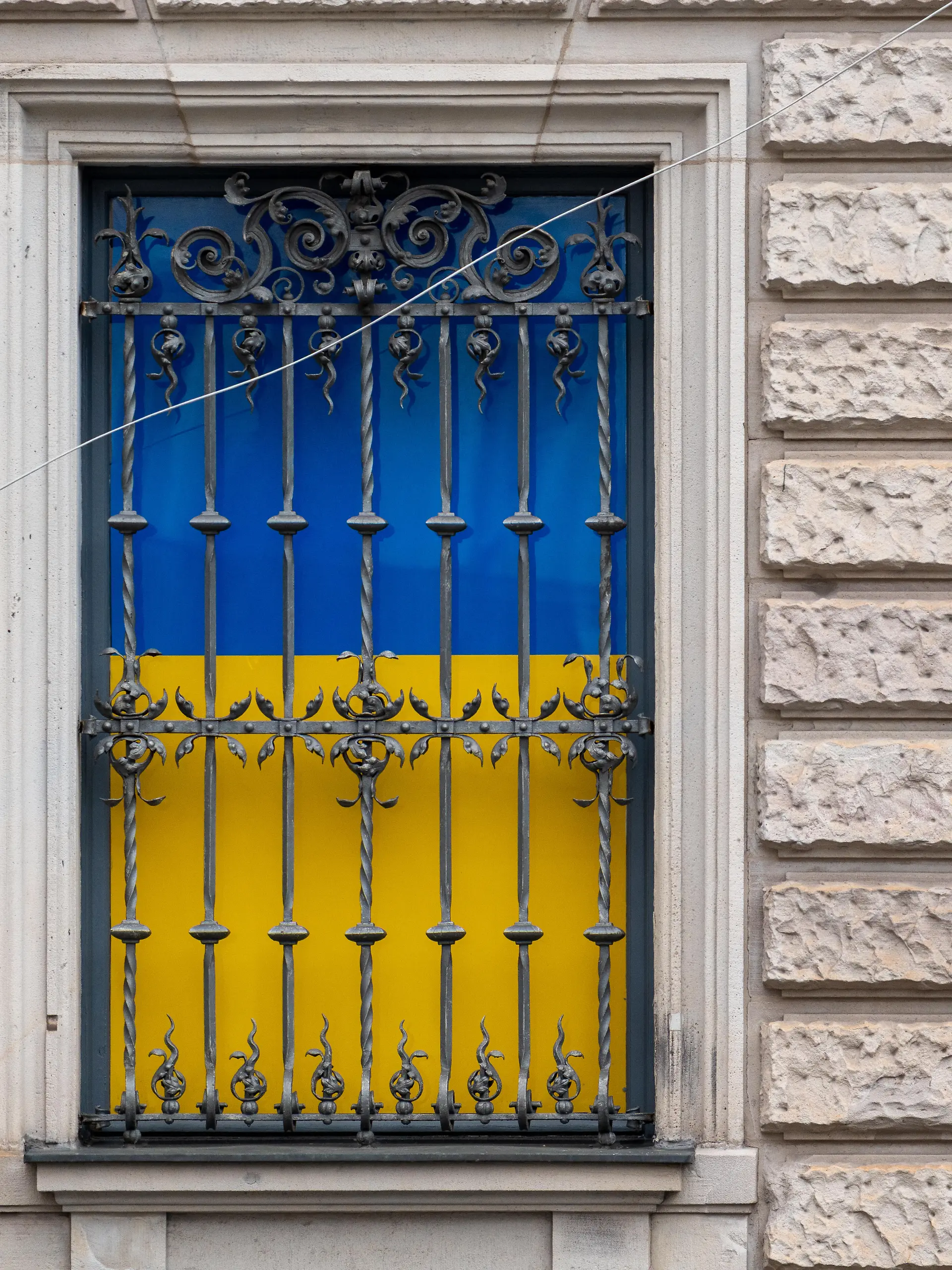 Fenster mit Metallgitter am Ukraine House während der Münchner Sicherheitskonferenz 2026. Hinter dem Gitter sind die Farben der ukrainischen Flagge sichtbar