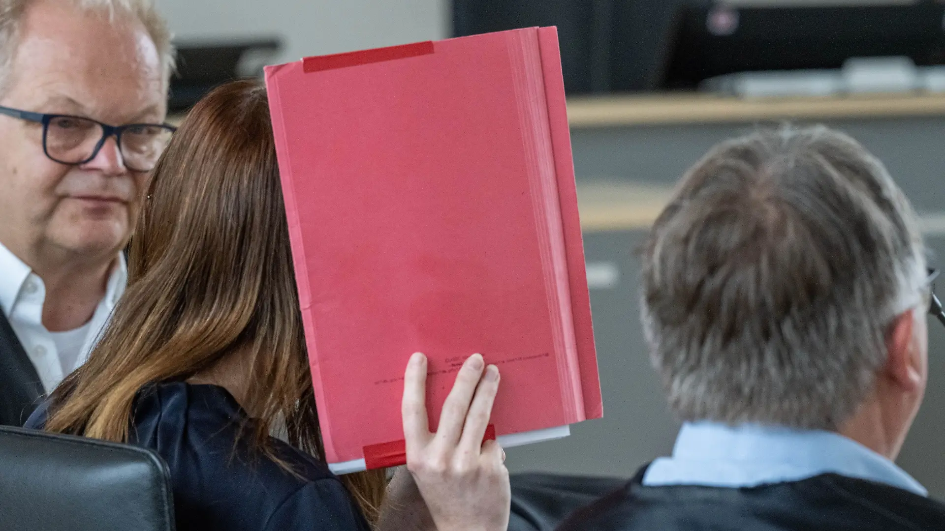 18.06.2026, Mecklenburg-Vorpommern, Rostock: Die Angeklagte (M) verdeckt ihr Gesicht mit einem Hefter und sitzt neben Thomas Löcker, Anwalt, im Saal des Landgerichts zu Beginn der Fortsetzung des Mordprozesses im Fall Fabian. Der Angeklagten wird vorgeworfen am 10.10.2025 heimtückisch und aus niedrigen Beweggründen den zur Tatzeit achtjährigen Fabian aus Güstrow getötet zu haben.