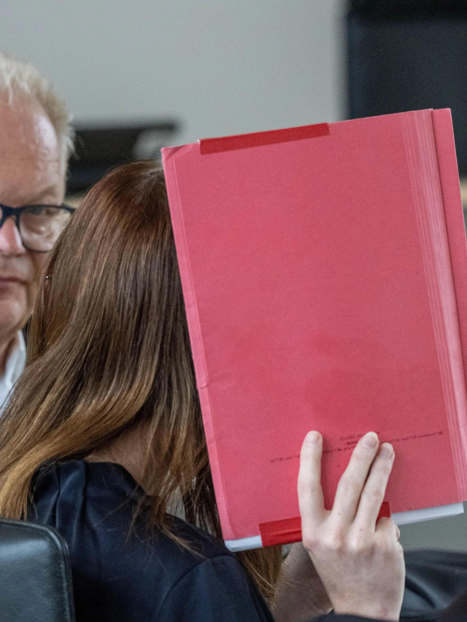 18.06.2026, Mecklenburg-Vorpommern, Rostock: Die Angeklagte (M) verdeckt ihr Gesicht mit einem Hefter und sitzt neben Thomas Löcker, Anwalt, im Saal des Landgerichts zu Beginn der Fortsetzung des Mordprozesses im Fall Fabian. Der Angeklagten wird vorgeworfen am 10.10.2025 heimtückisch und aus niedrigen Beweggründen den zur Tatzeit achtjährigen Fabian aus Güstrow getötet zu haben.