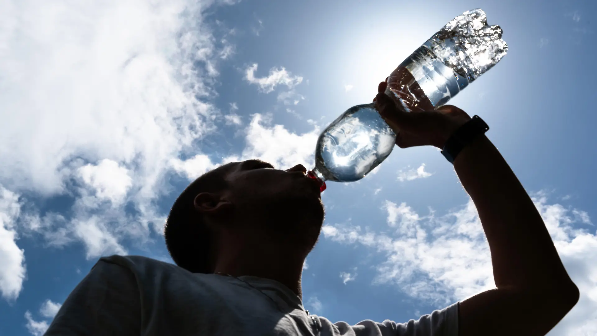 Eine Person trinkt Wasser unter direkter Sonneneinstrahlung an einem heißen Sommertag. Symbolfoto für die Bedeutung ausreichender Flüssigkeitszufuhr bei Hitze, Hitzewellen und zunehmenden klimatischen Belastungen