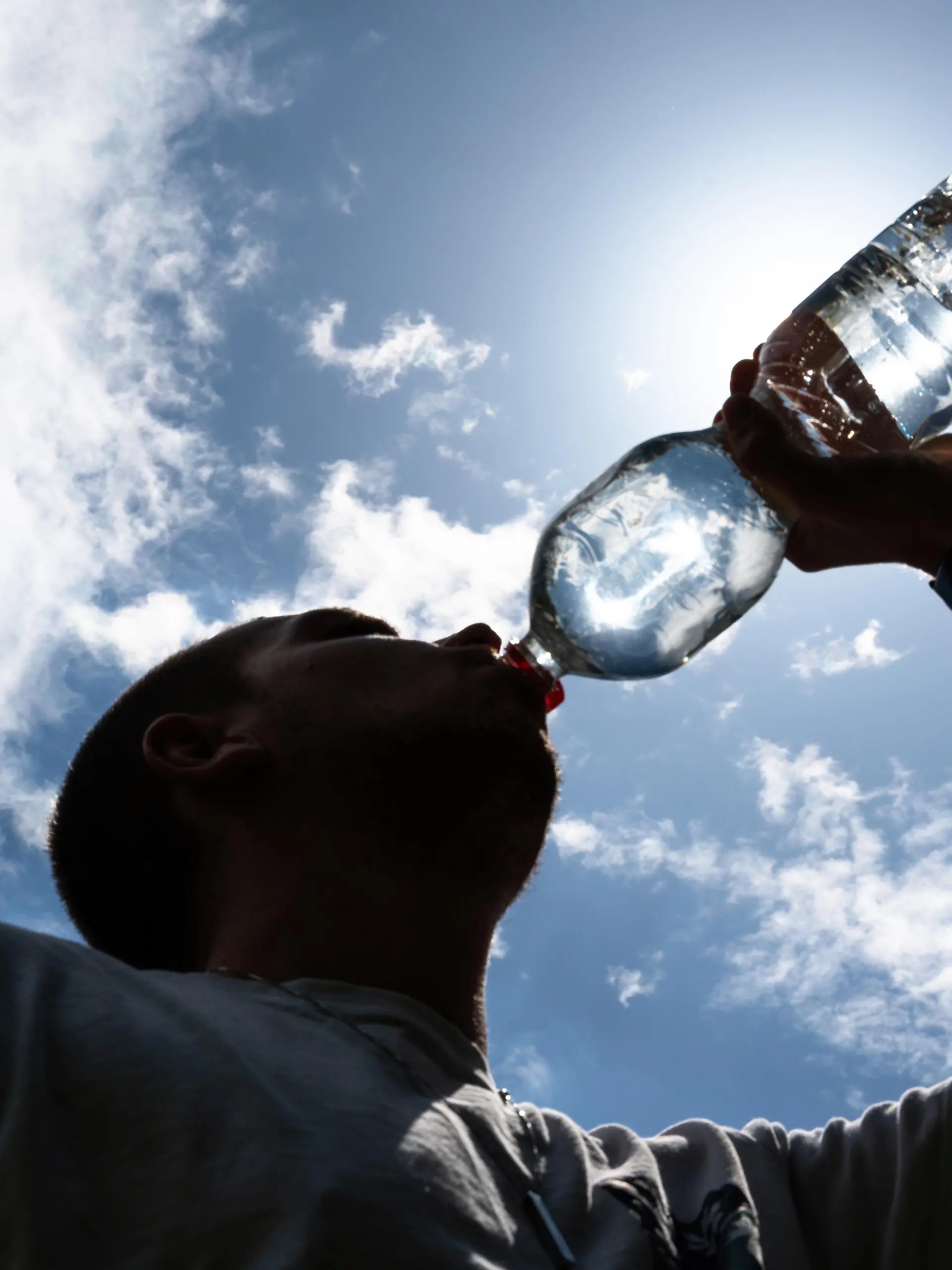 Eine Person trinkt Wasser unter direkter Sonneneinstrahlung an einem heißen Sommertag. Symbolfoto für die Bedeutung ausreichender Flüssigkeitszufuhr bei Hitze, Hitzewellen und zunehmenden klimatischen Belastungen