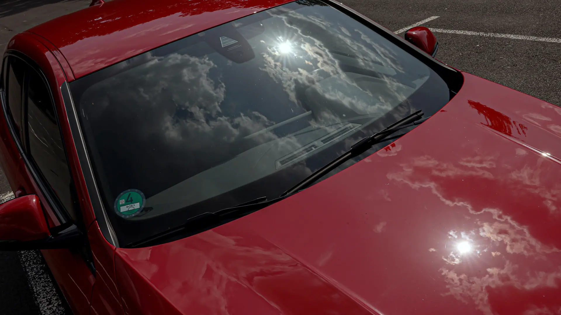 Ein erneut sehr heisser (heißer) Tag im Siegerland. Das Sommerwetter geht weiter. Ein rotes Auto steht in der Sonne auf einem Parkplatz und heizt sich auf. Die Sonne und Wolken spiegeln sich in der Frontscheibe und am Fahrzeuglack. Wer bei diesen Temperaturen ein Kind oder Hund im Fahrzeug zuruecklaesst (zurücklässt) handelt verantwortungslos. Symbolbild erhitztes Auto am 14.08.2025 in Siegen/Deutschland.