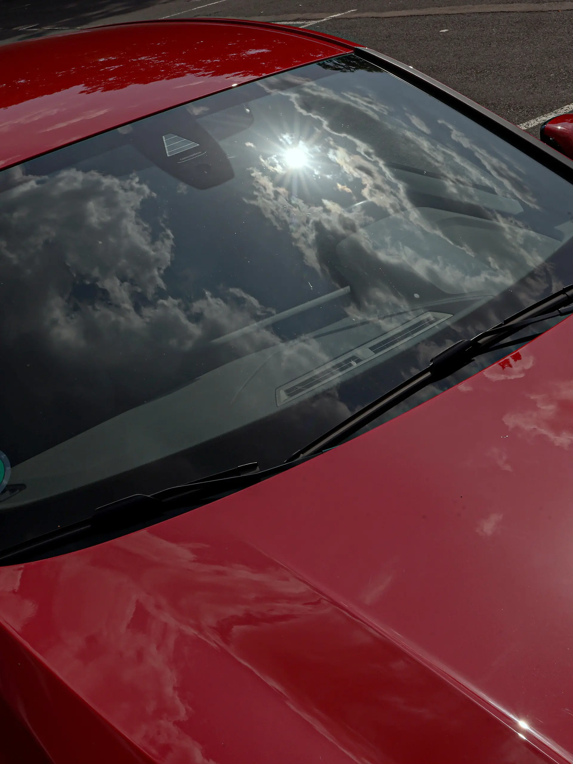 Ein erneut sehr heisser (heißer) Tag im Siegerland. Das Sommerwetter geht weiter. Ein rotes Auto steht in der Sonne auf einem Parkplatz und heizt sich auf. Die Sonne und Wolken spiegeln sich in der Frontscheibe und am Fahrzeuglack. Wer bei diesen Temperaturen ein Kind oder Hund im Fahrzeug zuruecklaesst (zurücklässt) handelt verantwortungslos. Symbolbild erhitztes Auto am 14.08.2025 in Siegen/Deutschland.