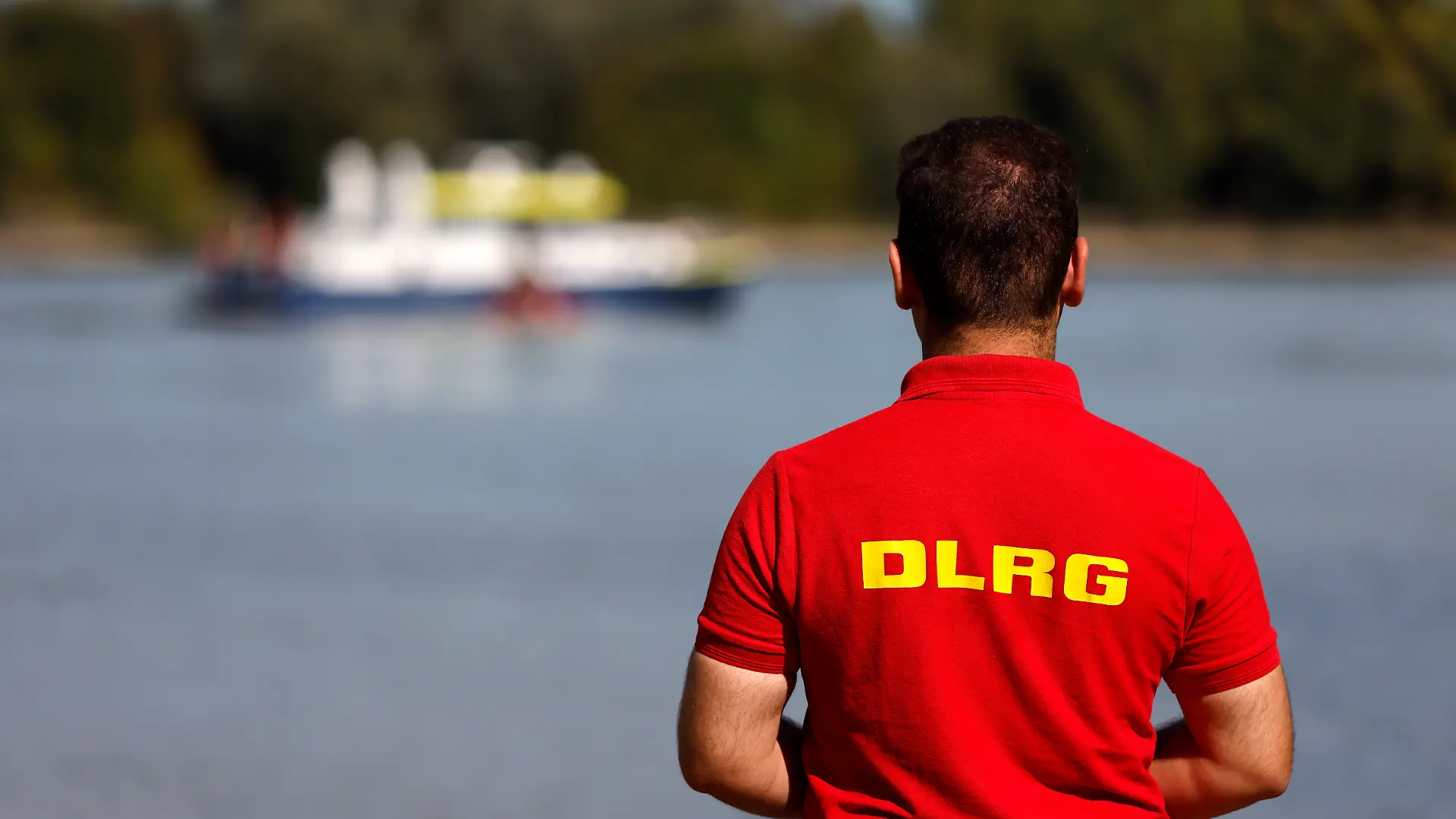 Ein Mitarbeiter der DLRG steht am Rheinufer, im Hintergrund ein Boot der Wasserschutzpolizei. Mitarbeiter des Ordnungsamts der Stadt Köln informieren derzeit am Rheinufer über die neuen Badeverbot-Regeln und sind an der Rodenkirchener Riviera präsent. Bei Verstößen sollen künftig bis zu 1000 Euro Bußgeld fällig sein. (Themenbild, Symbolbild) Köln, 19.09.2025