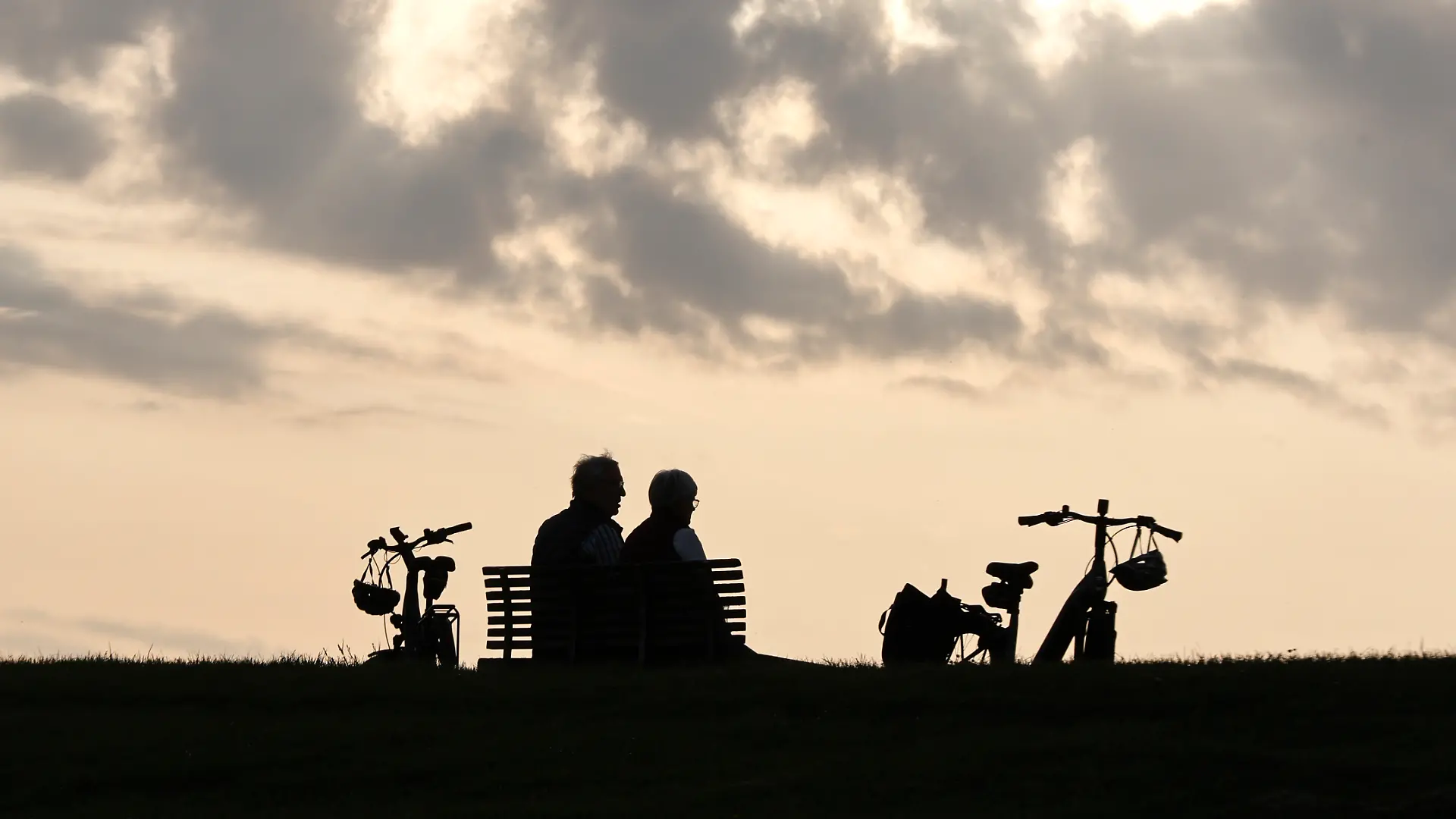 Ein Rentnerpaar macht eine Pause von ihrer e-bike Tour und sitztzum Sonnenuntergan auf einer Parkbank, Neuharlingersiel, 23.05.2026.