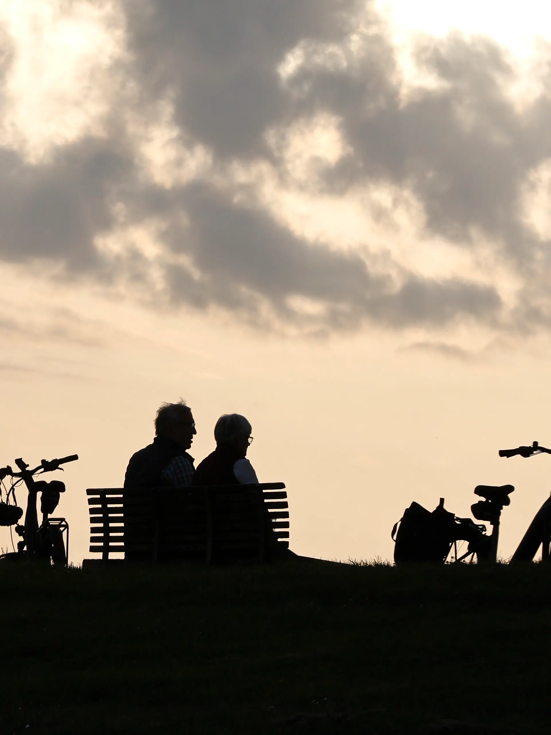 Ein Rentnerpaar macht eine Pause von ihrer e-bike Tour und sitztzum Sonnenuntergan auf einer Parkbank, Neuharlingersiel, 23.05.2026.