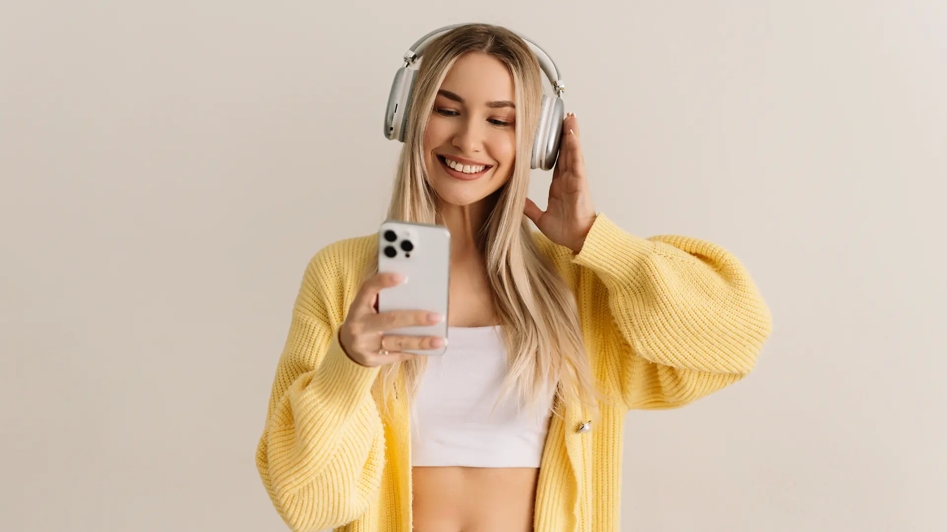 Eine junge Frau in einem gelben Pullover hört mit kabellosen Kopfhörern Musik.