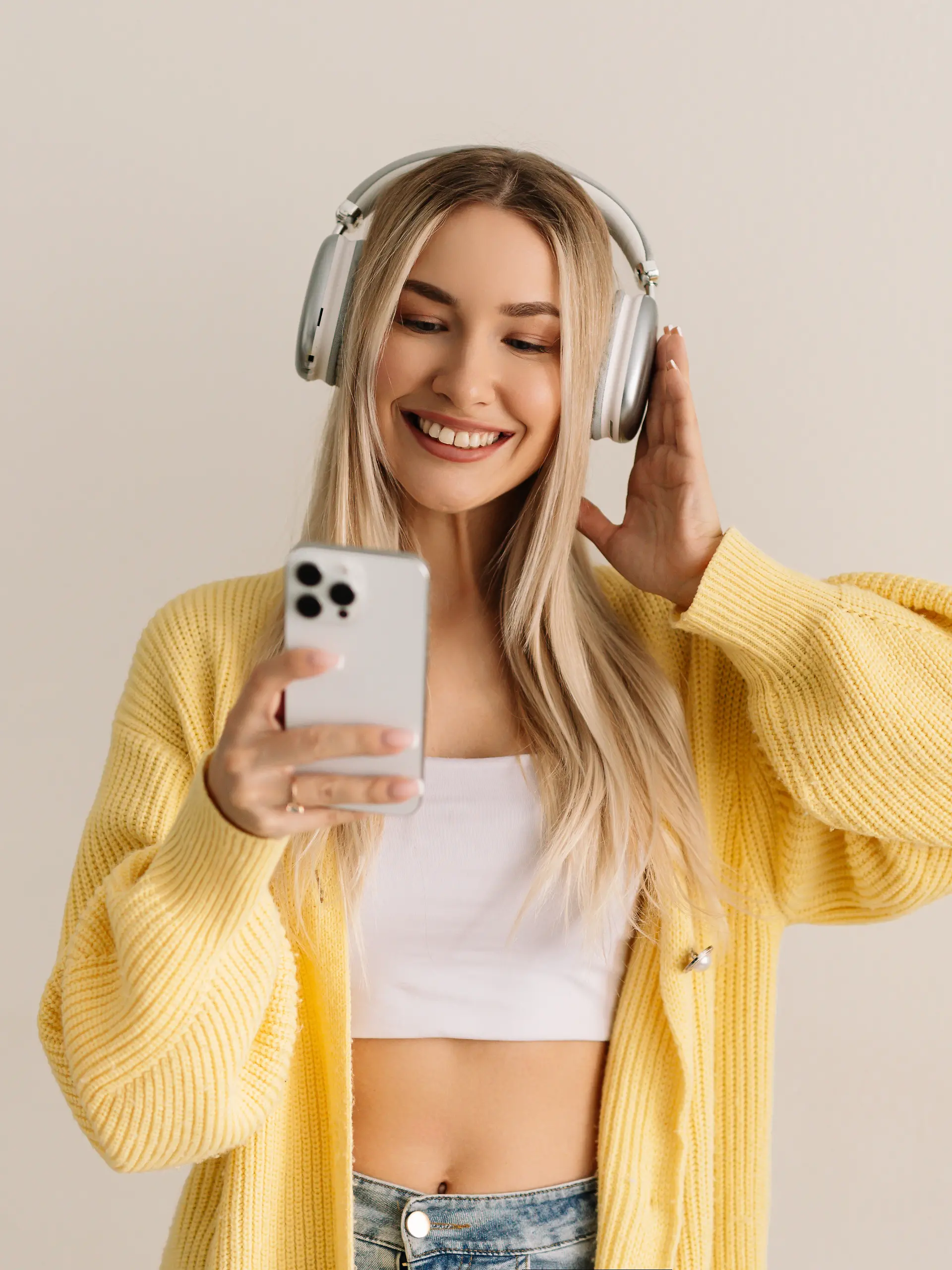 Eine junge Frau in einem gelben Pullover hört mit kabellosen Kopfhörern Musik.