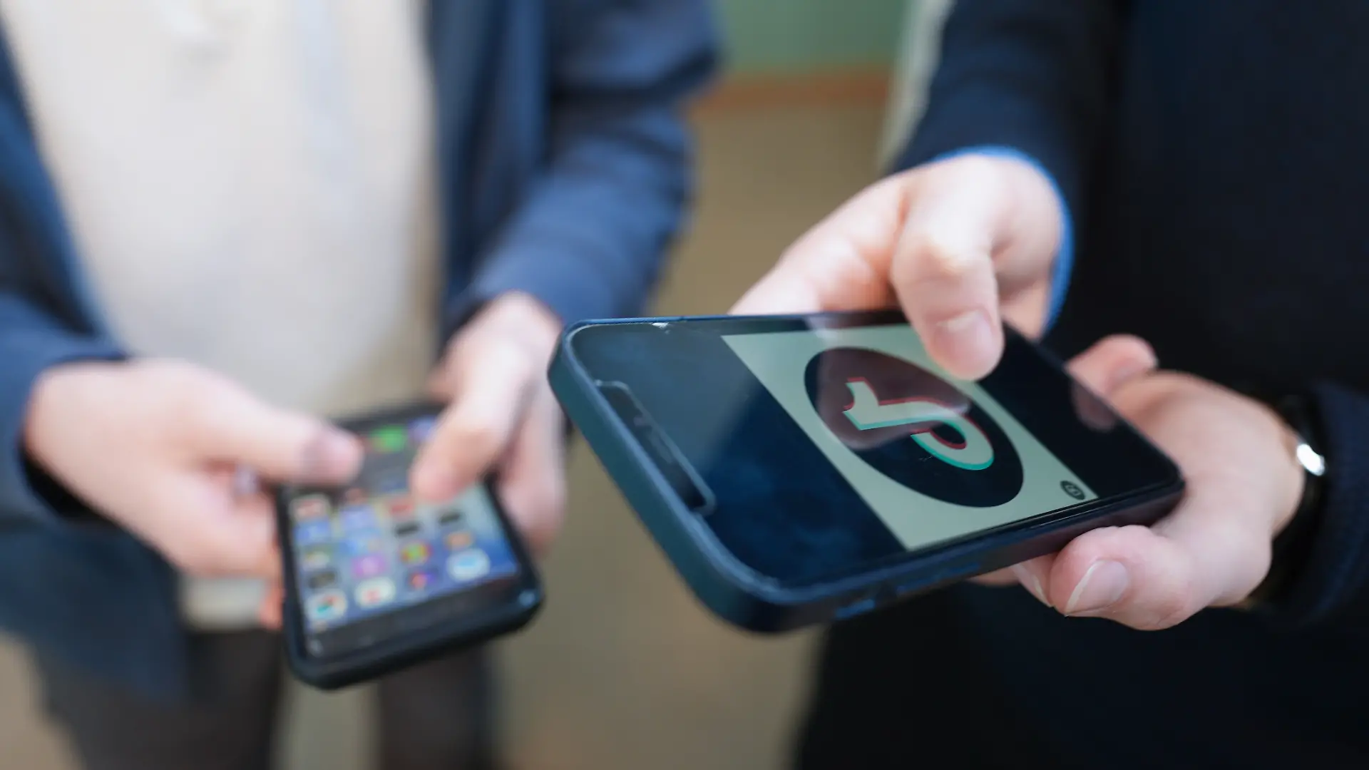 Zwei Schüler stehen vor einem Klassenraum im Goethe-Gymnasium und schauen auf ihre Smartphones, auf einem der Displays ist das Logo der Social-Media-Plattform TikTok zu sehen. Aktuell wird in Deutschland über Altersgrenzen für soziale Medien sowie über mögliche strengere Regeln zur Handynutzung an Schulen diskutiert.