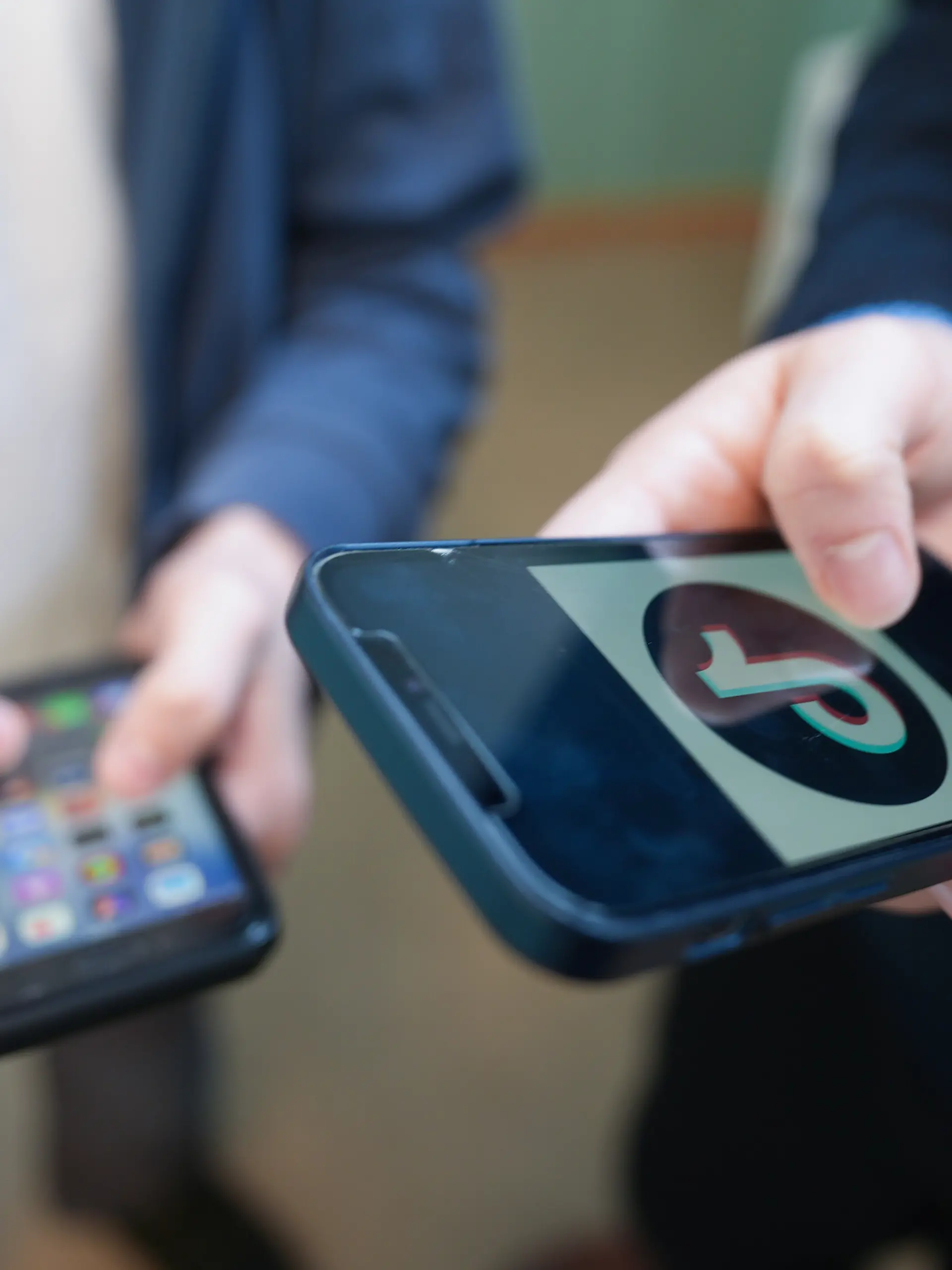 Zwei Schüler stehen vor einem Klassenraum im Goethe-Gymnasium und schauen auf ihre Smartphones, auf einem der Displays ist das Logo der Social-Media-Plattform TikTok zu sehen. Aktuell wird in Deutschland über Altersgrenzen für soziale Medien sowie über mögliche strengere Regeln zur Handynutzung an Schulen diskutiert.