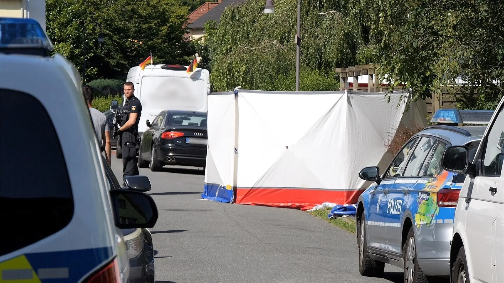 Kräfte der Polizei sind im Ortsteil Fähr-Lobbendorf auf der Straße im Einsatz, auf der ein Mann mit tödlichen Stich- und Schnittverletzungen gefunden wurde. Eine tote Frau wurde im Keller eines Mehrparteienhauses entdeckt. Die Polizei geht nach eigenen Angaben davon aus, dass sie Opfer eines Gewaltverbrechens wurden und fahndet nach dem Täter.