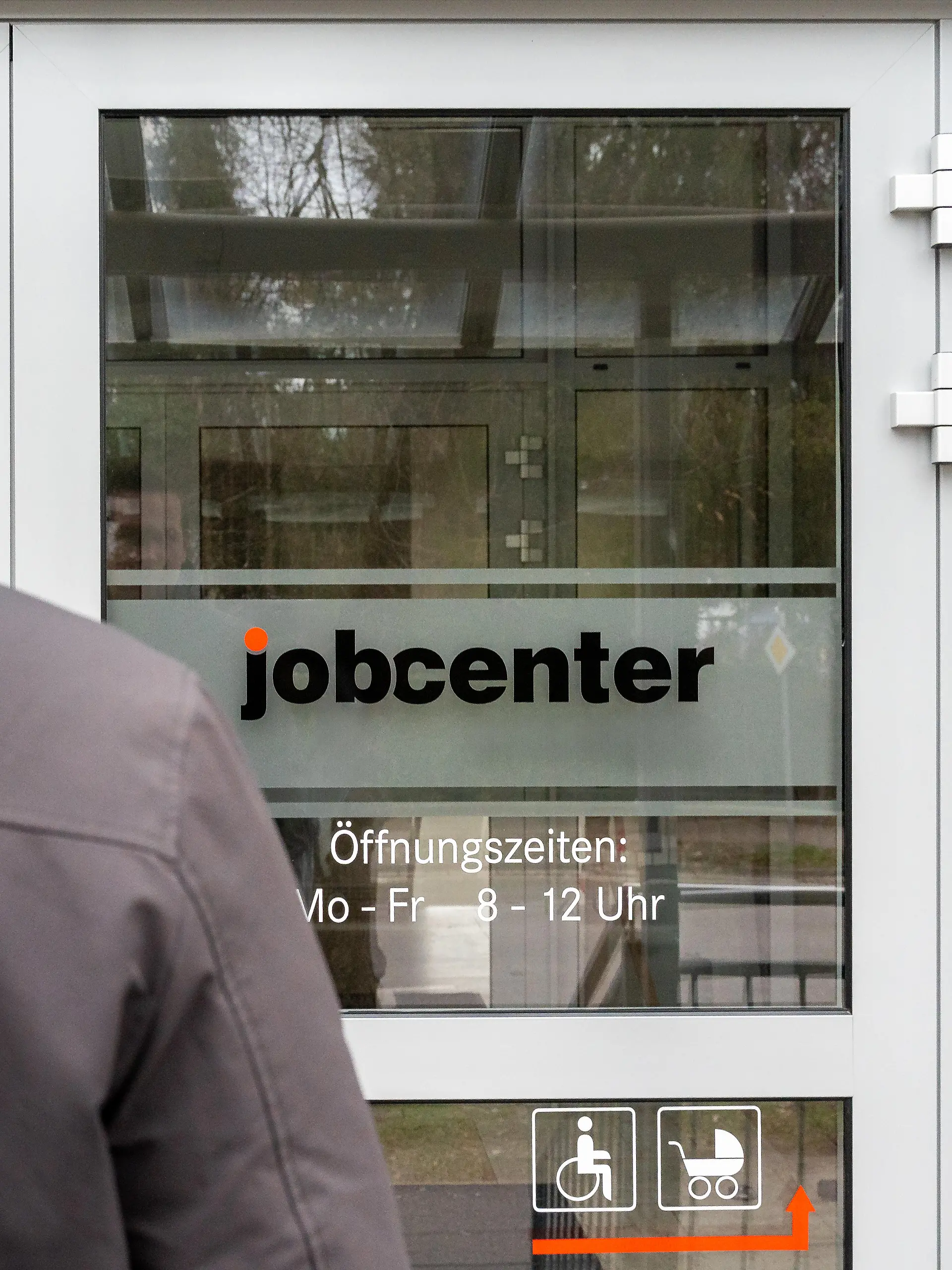 Ein junger Mann steht vor dem Eingang eines Jobcenters.