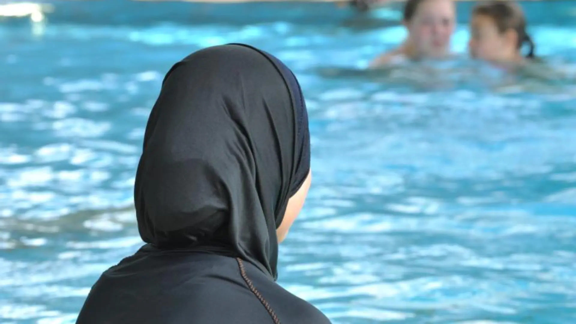 Frau sitzt mit Burkini am Schwimmbadrand
