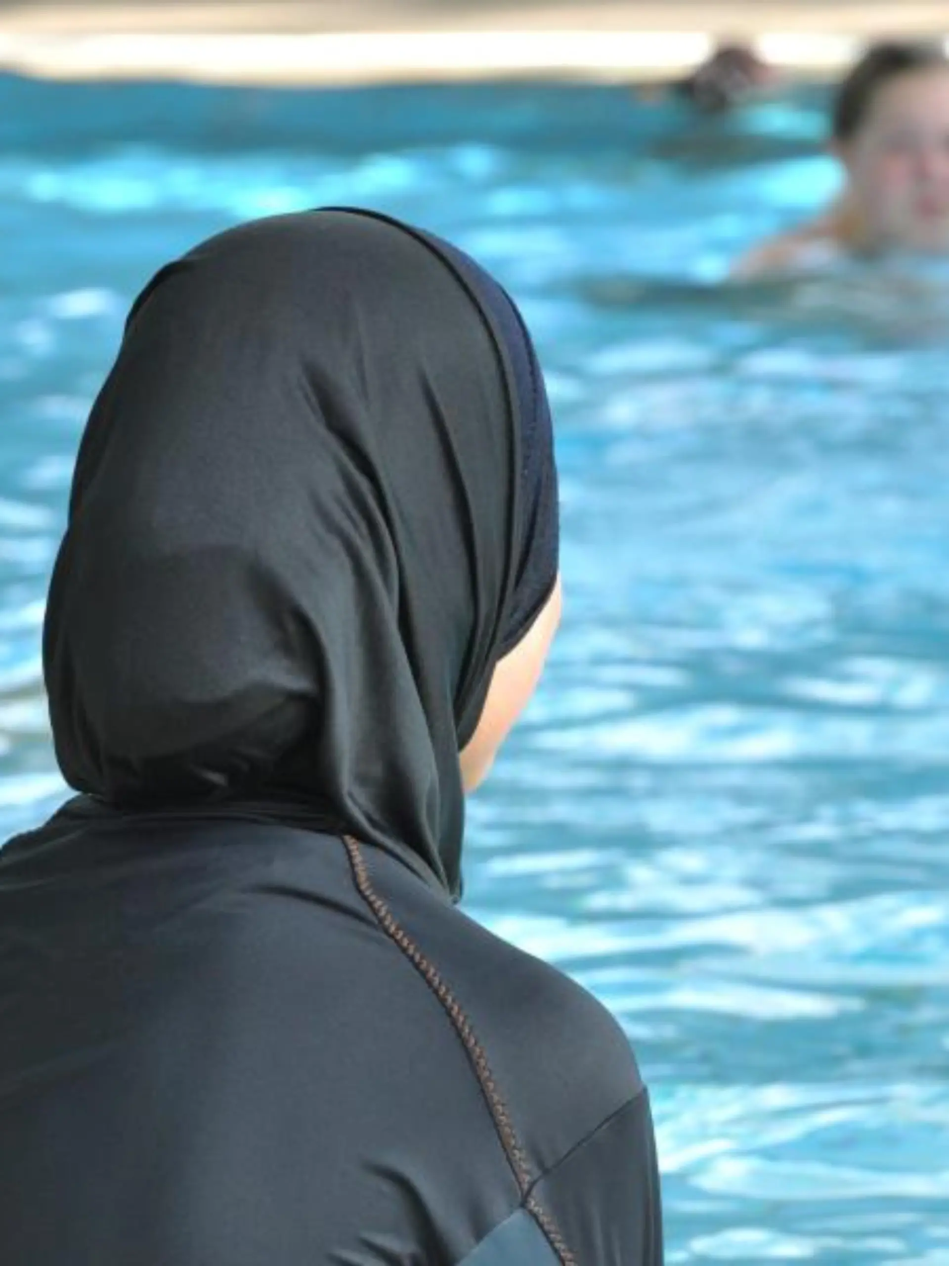 Frau sitzt mit Burkini am Schwimmbadrand