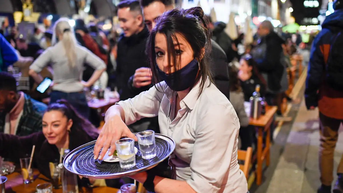 A waitress serves drinks at tables outside a pub in Soho, London, on the day some of England's coronavirus lockdown restrictions were eased by the British government, Monday, April 12, 2021. Pubs, shops and hairdressers have opened as lockdown restrictions are eased Monday. (AP Photo/Alberto Pezzali)