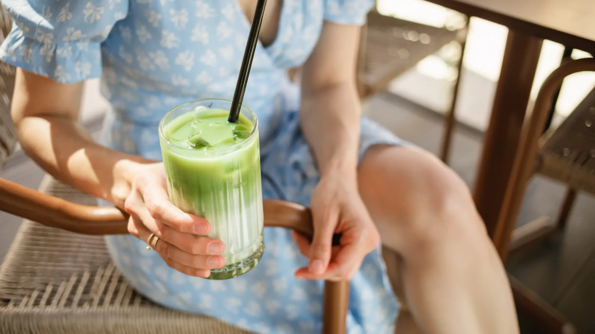 Frau trägt ein Blümchenkleid und trinkt einen Iced Matcha Latte.