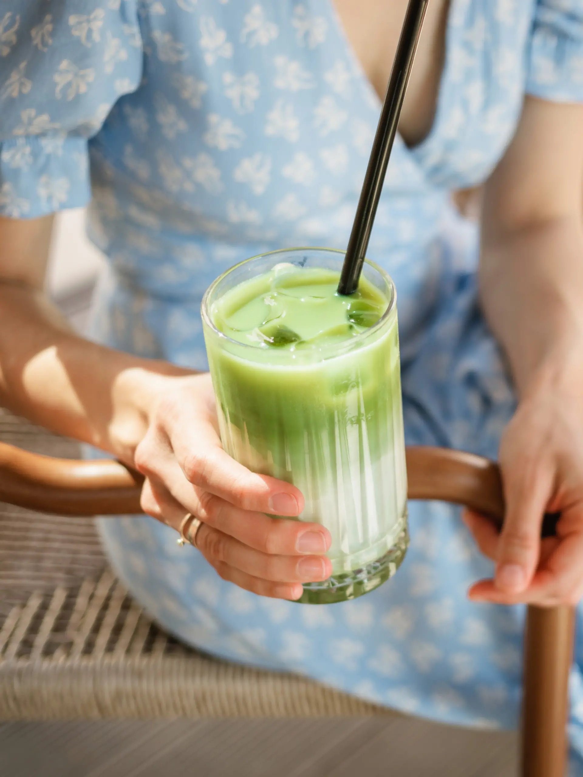 Frau trägt ein Blümchenkleid und trinkt einen Iced Matcha Latte.