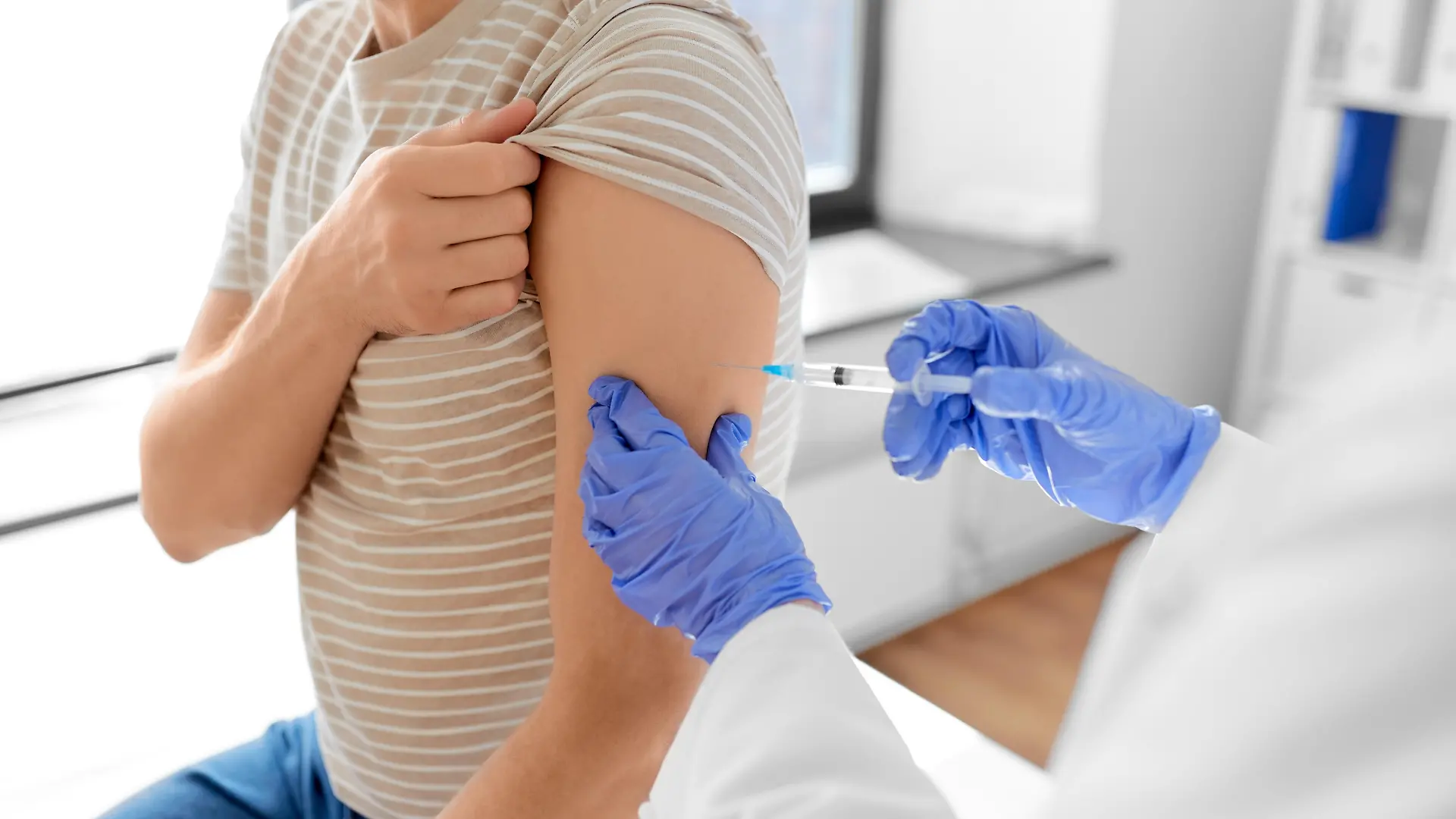 health, medicine and pandemic concept - female doctor or nurse wearing protective medical mask and gloves with syringe vaccinating male patient at hospital || Modellfreigabe vorhanden