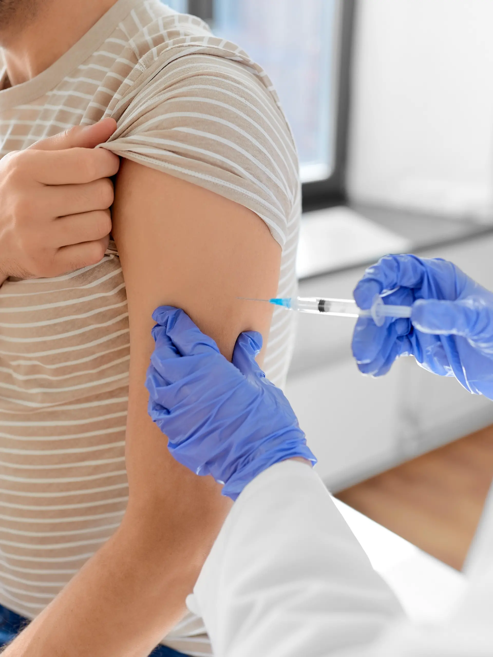 health, medicine and pandemic concept - female doctor or nurse wearing protective medical mask and gloves with syringe vaccinating male patient at hospital || Modellfreigabe vorhanden