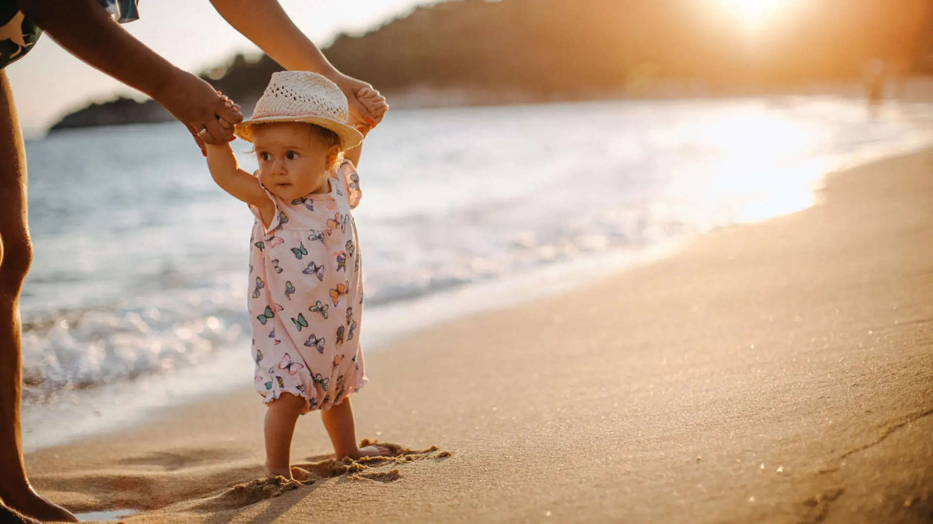 Kleinkind läuft an den Händen der Mutter am Strand