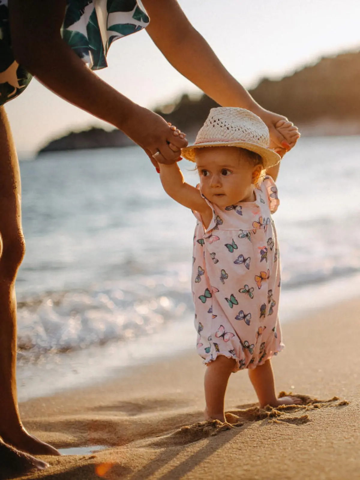 Kleinkind läuft an den Händen der Mutter am Strand