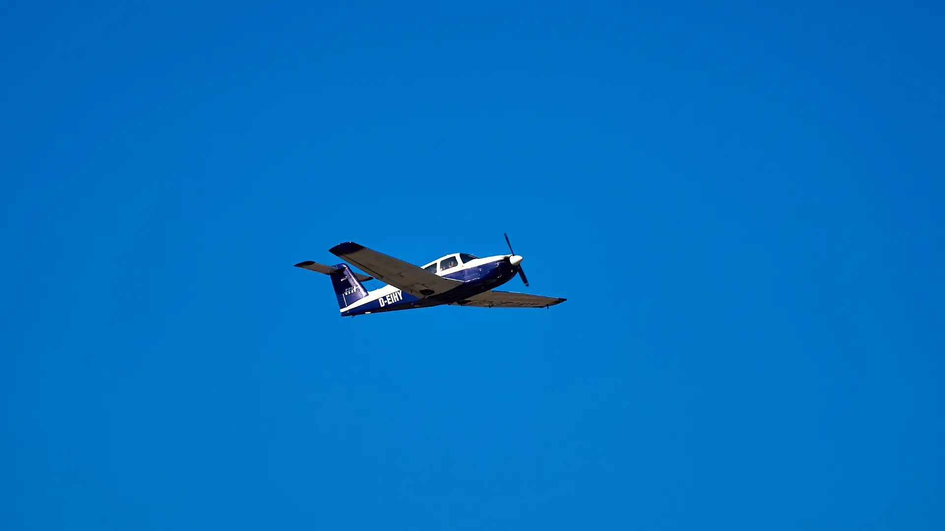 Ein einmotoriges Propellerflugzeug vom Typ Piper PA-28 Cherokee im Flug über klarem, blauem Himmel. Das Leichtflugzeug ist besonders beliebt für Flugtraining, Privatflüge und Sportfliegerei.