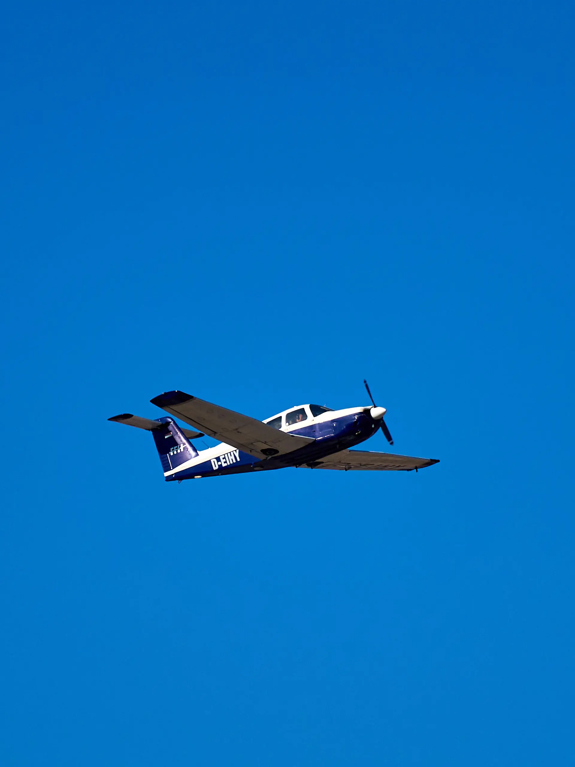 Ein einmotoriges Propellerflugzeug vom Typ Piper PA-28 Cherokee im Flug über klarem, blauem Himmel. Das Leichtflugzeug ist besonders beliebt für Flugtraining, Privatflüge und Sportfliegerei.