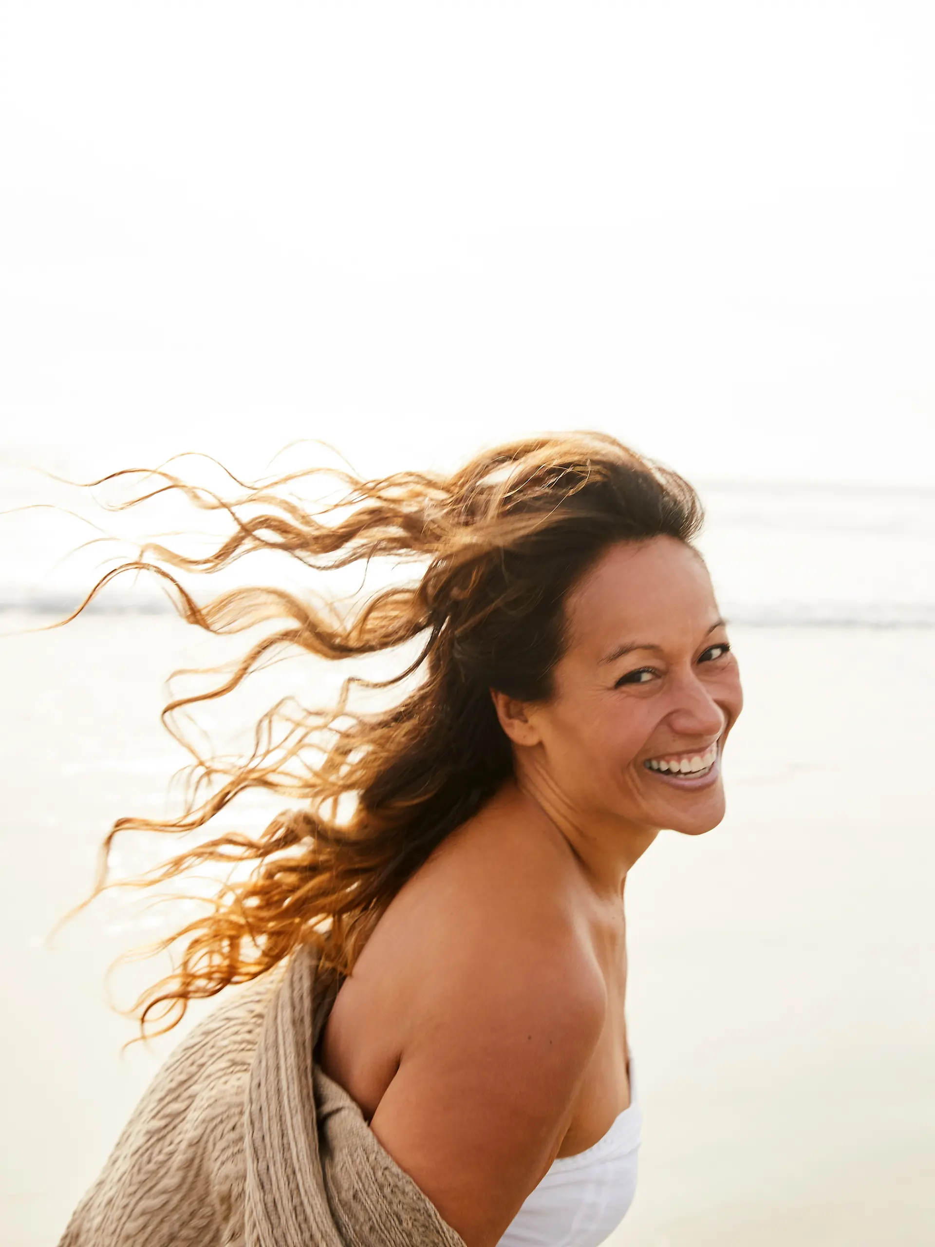 Lachende Frau zu Fuß an einem Strand an einem luftigen Nachmittag