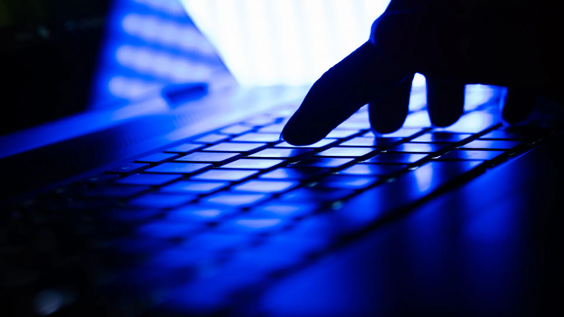 Hand auf einer Laptop Tastatur in einem dunklen Raum