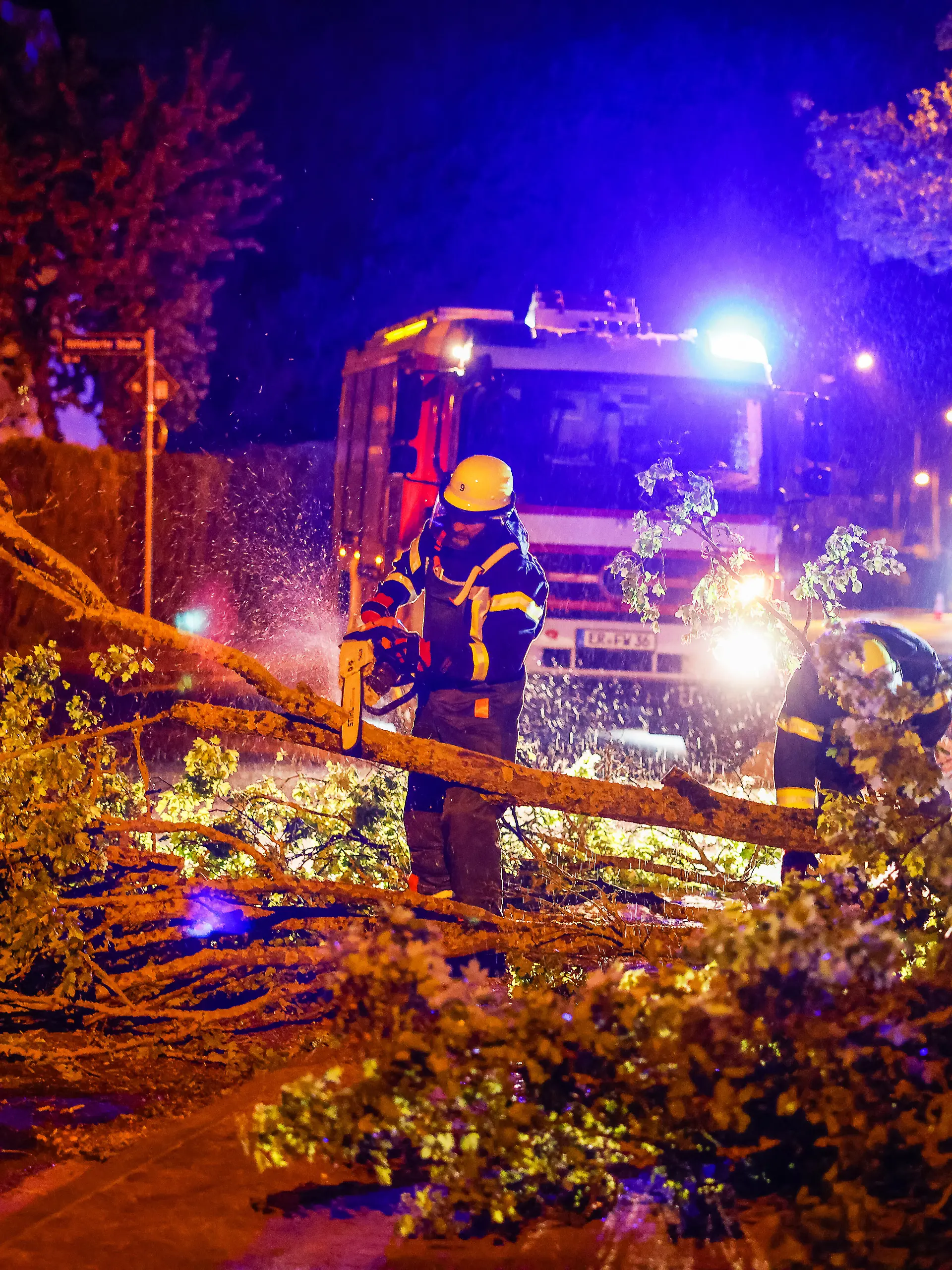 Einsatzkräfte der Feuerwehr zersägen mit einer Kettensäge einen umgestürzten Baum auf einer Straße im Regierungsbezirk Mittelfranken. Das über Deutschland hinweggezogene Unwetter hat am Montagabend in Teilen des Landes unter anderem Bäume umstürzen lassen und Dächer abgedeckt. +++ dpa-Bildfunk +++