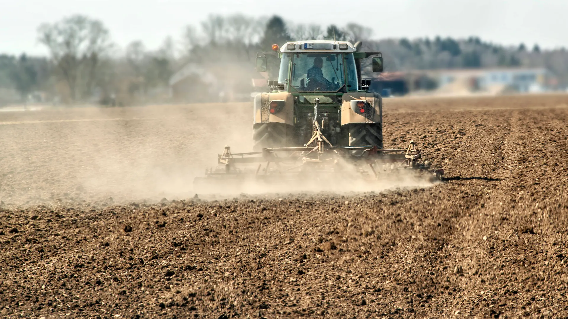 Landwirt mit Traktor auf dem Acker, wirbelt Staubwolken au