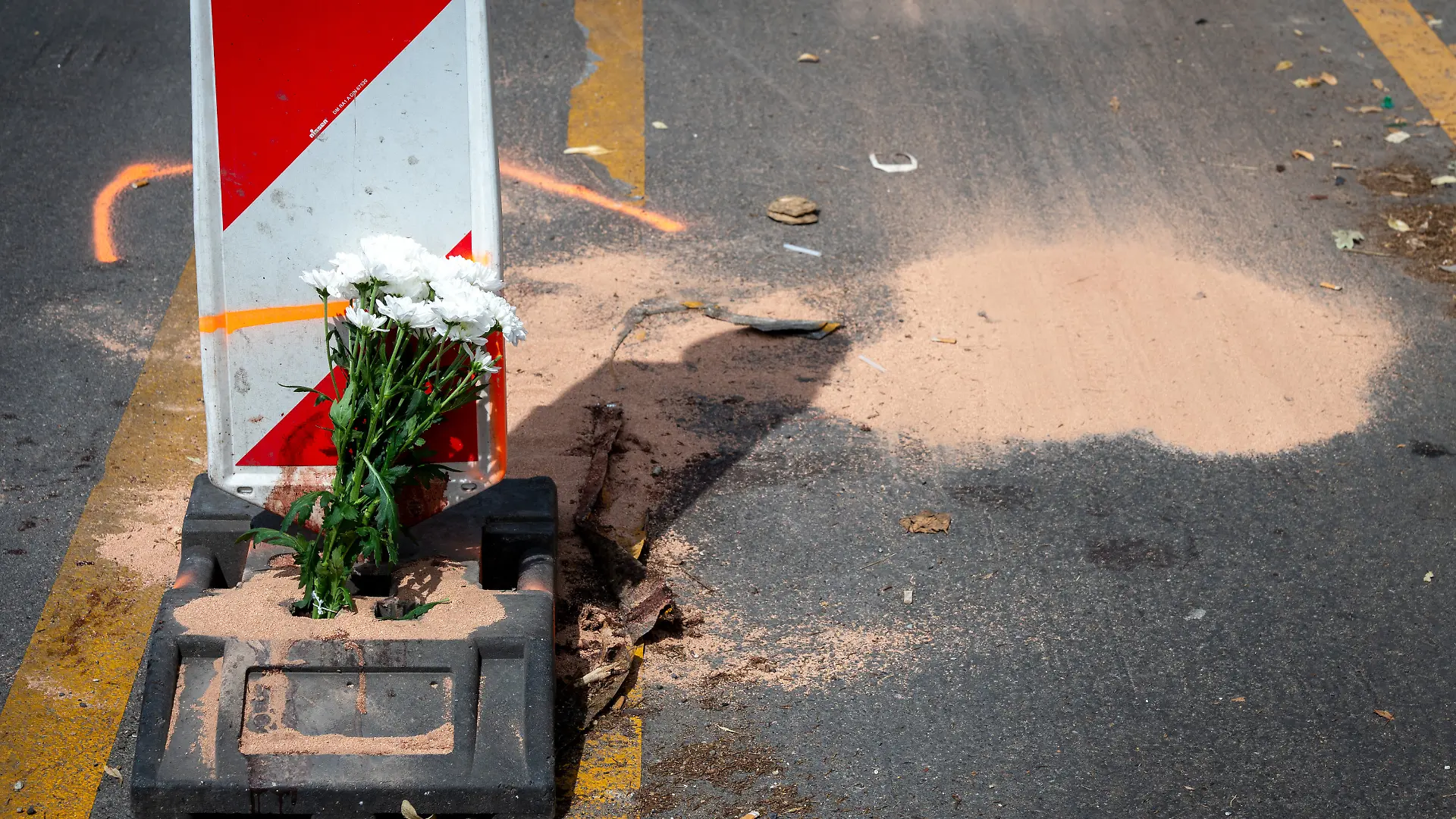 15.07.2026, Berlin: Blumen stehen an der Kreuzung Urbanstraße/Ecke Blücherstraße in Kreuzberg vor einer aufgemalten Markierung und einer kleinen Menge gestreutem Bindemittel. Hier starb in der vergangenen Nacht der Fahrer eines E-Scooters bei einem Unfall. Foto: Soeren Stache/dpa +++ dpa-Bildfunk +++