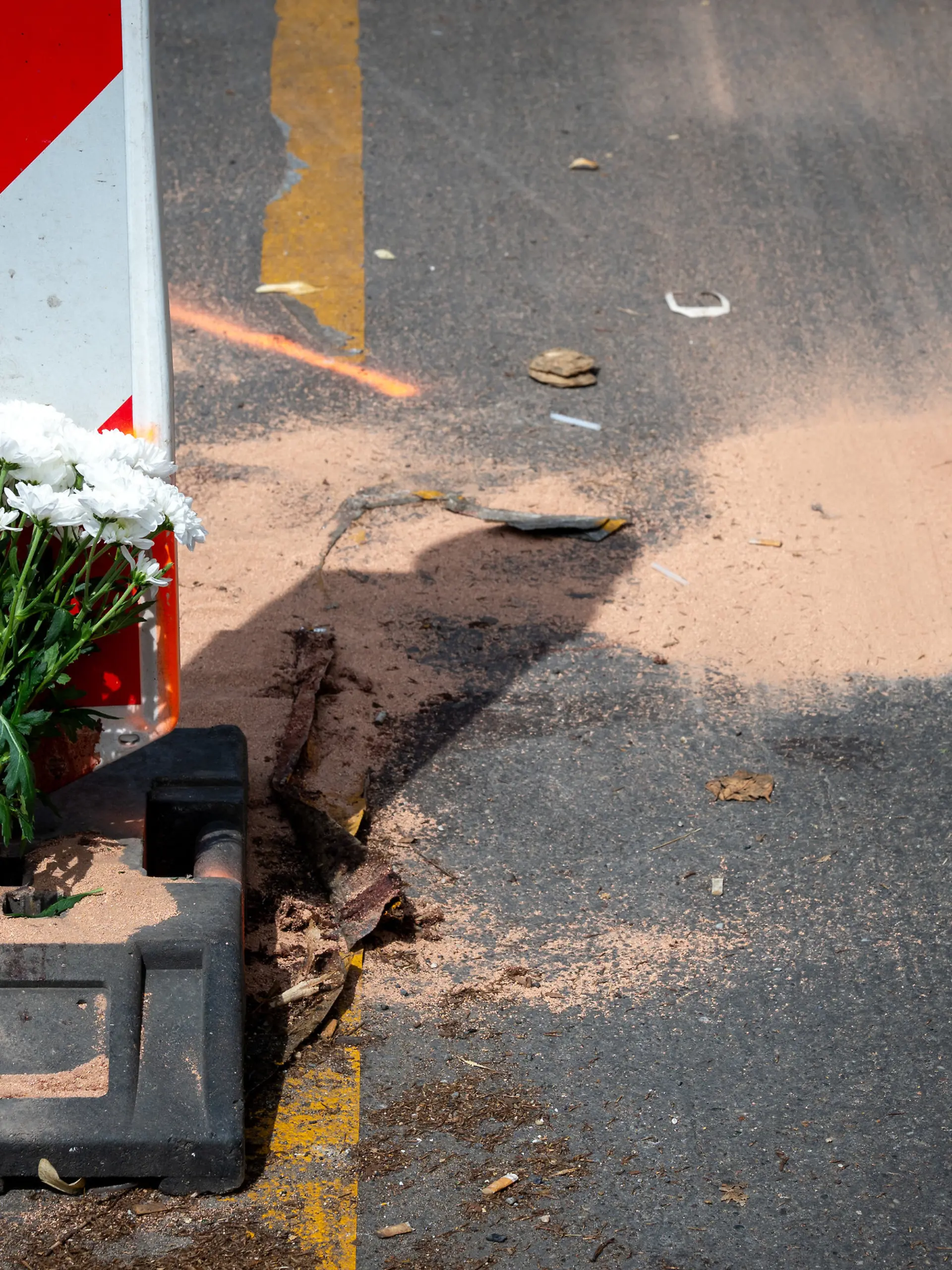 15.07.2026, Berlin: Blumen stehen an der Kreuzung Urbanstraße/Ecke Blücherstraße in Kreuzberg vor einer aufgemalten Markierung und einer kleinen Menge gestreutem Bindemittel. Hier starb in der vergangenen Nacht der Fahrer eines E-Scooters bei einem Unfall. Foto: Soeren Stache/dpa +++ dpa-Bildfunk +++