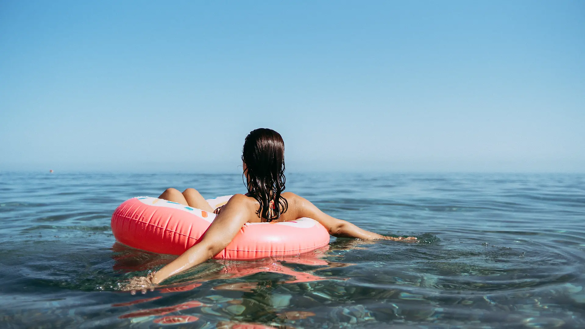 Junge Frau in einem Donut mit Streuseln am Strand. Sonnenuntergang im Sommer
