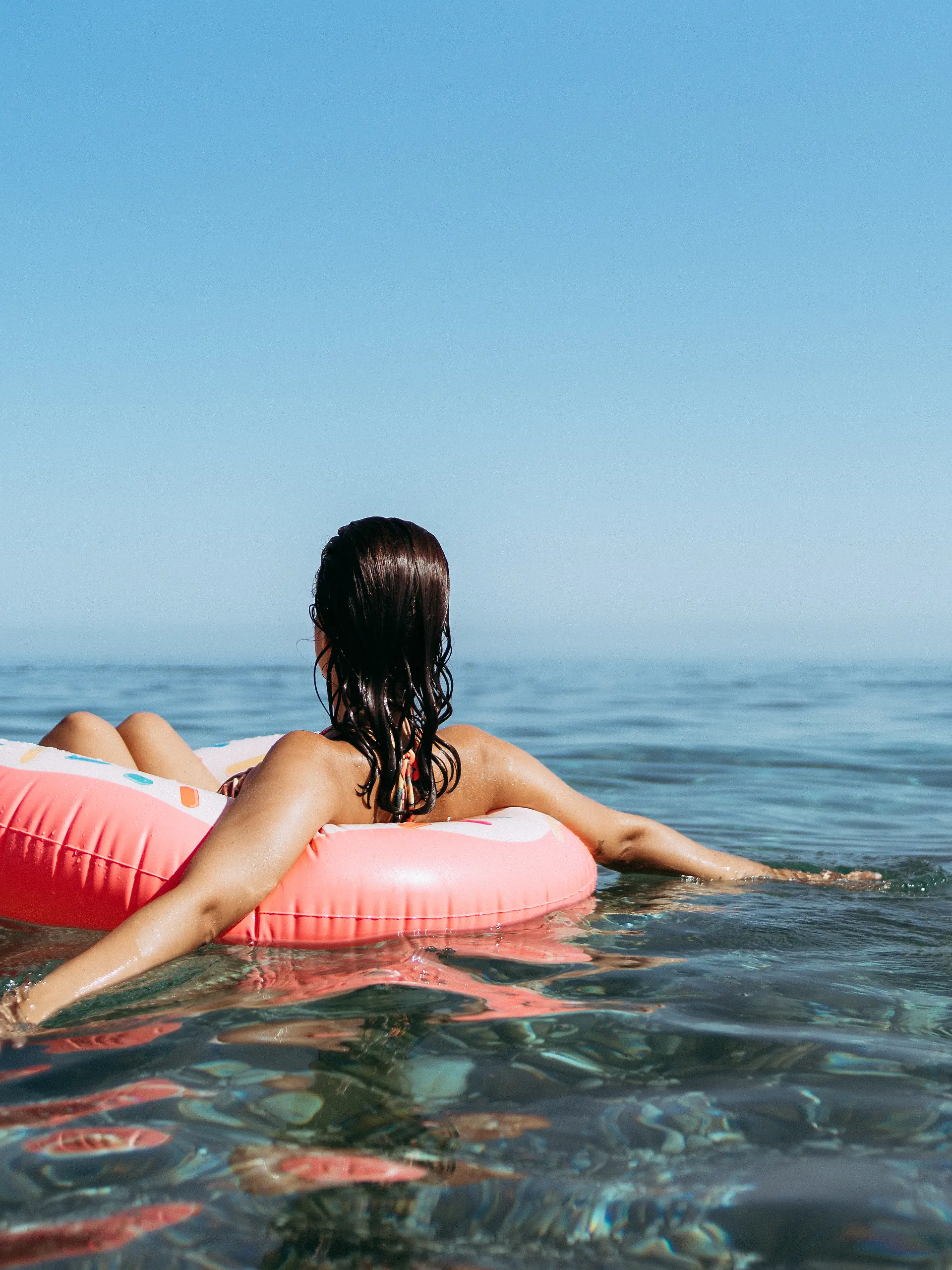 Junge Frau in einem Donut mit Streuseln am Strand. Sonnenuntergang im Sommer