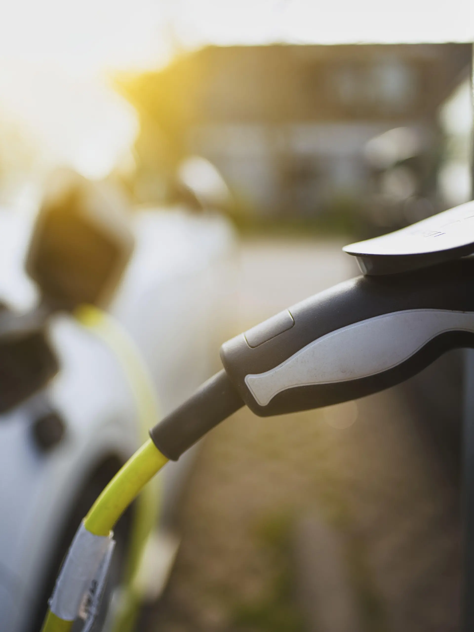 E-Auto mit Ladekabel und Stromstecker an einer Ladesäule angeschlossen bei Sonnenaufgang im Gegenlicht in einem Wohngebiet an der Straße, Schagen, Nordholland, Niederlande