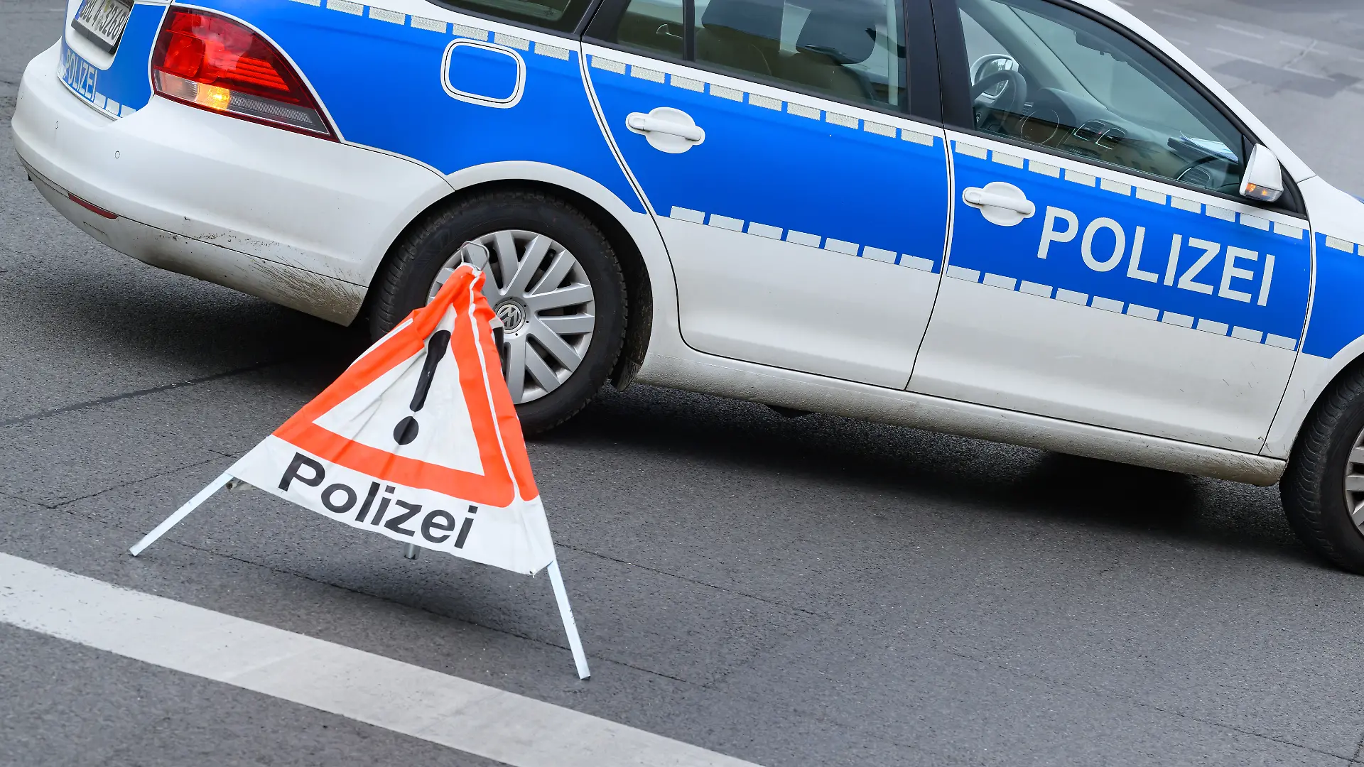 Ein Polizeifahrzeug steht zur Absicherung auf einer Straße. Im Vordergrund warnt ein aufgeklapptes, dreiseitiges Faltsignal mit einem roten Ausrufezeichen und der Aufschrift «Polizei» herannahende Verkehrsteilnehmer. Die temporäre Warnpyramide dient dem schnellen Schutz einer Einsatz- oder Unfallstelle im laufenden Straßenverkehr. (zu dpa: «16-Jährige stirbt bei Unfall auf A24 bei Neuruppin») +++ dpa-Bildfunk +++