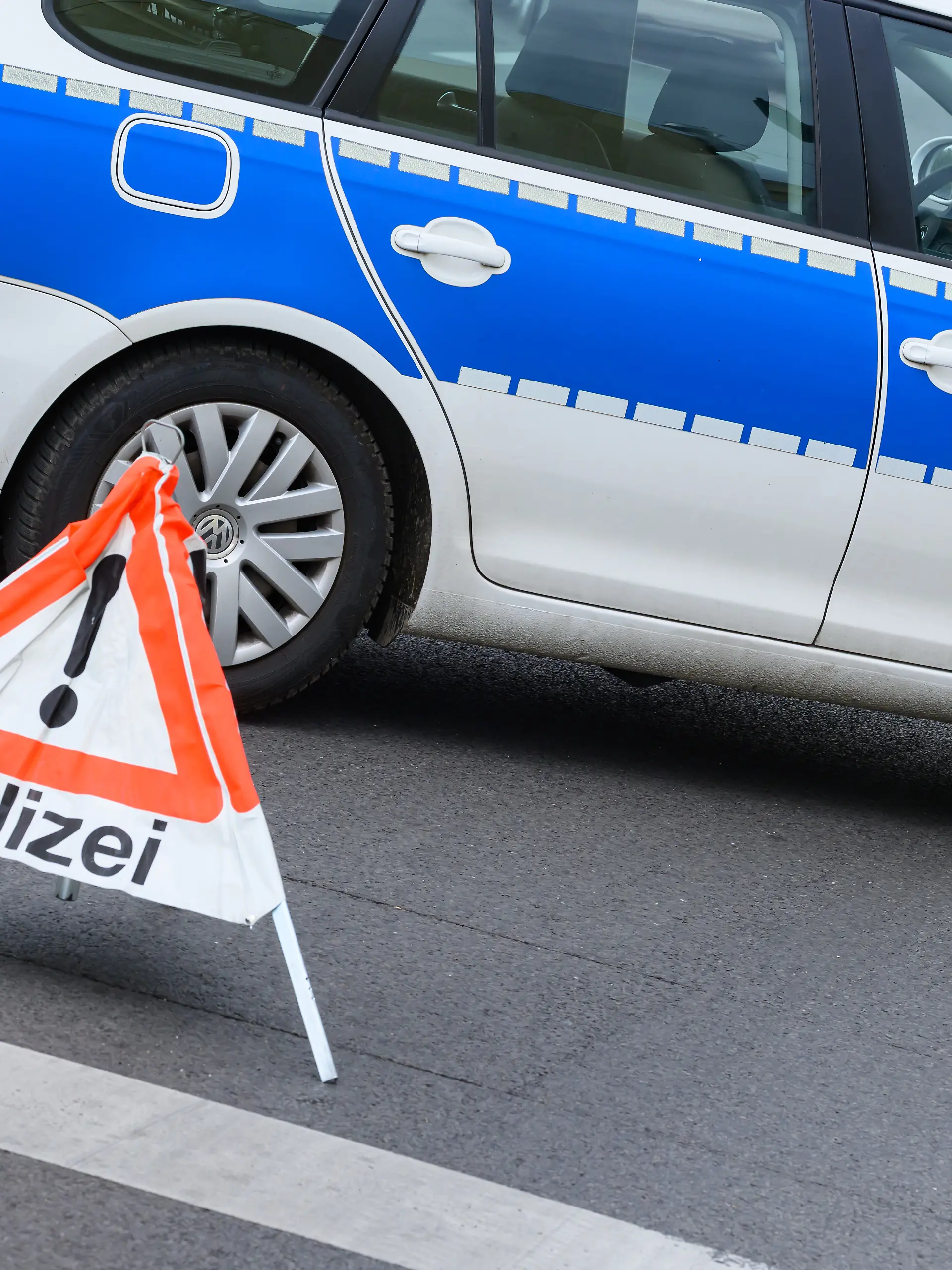 Ein Polizeifahrzeug steht zur Absicherung auf einer Straße. Im Vordergrund warnt ein aufgeklapptes, dreiseitiges Faltsignal mit einem roten Ausrufezeichen und der Aufschrift «Polizei» herannahende Verkehrsteilnehmer. Die temporäre Warnpyramide dient dem schnellen Schutz einer Einsatz- oder Unfallstelle im laufenden Straßenverkehr. (zu dpa: «16-Jährige stirbt bei Unfall auf A24 bei Neuruppin») +++ dpa-Bildfunk +++