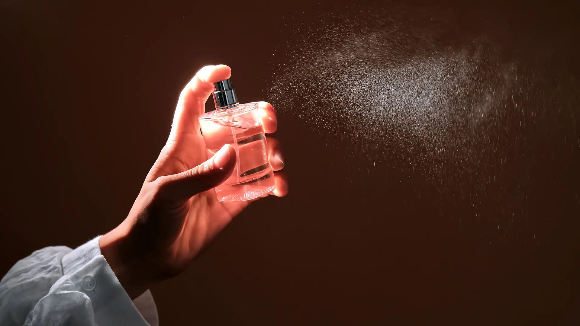 Eine Person sprüht mit einer Parfum-Flasche.