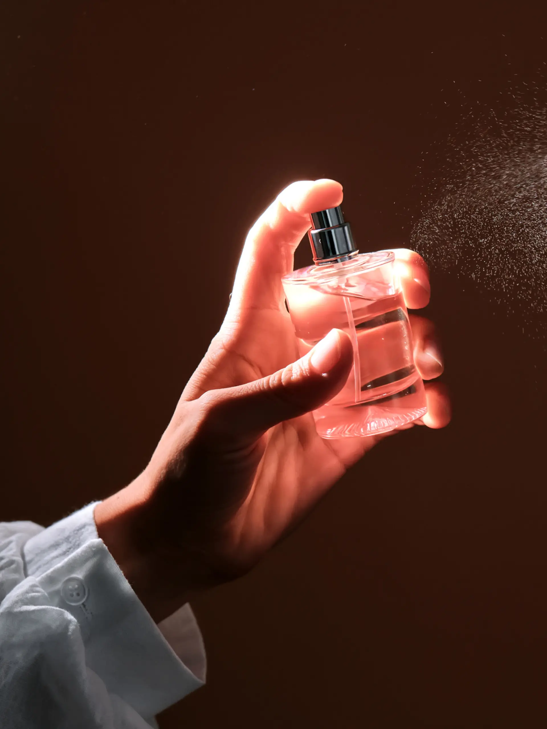 Eine Person sprüht mit einer Parfum-Flasche.