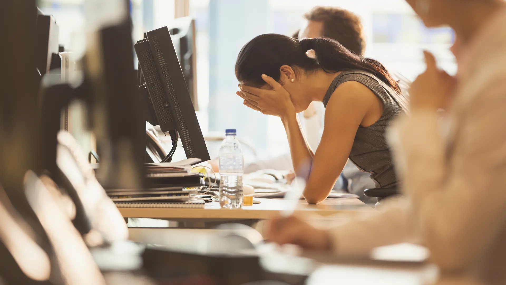Gestresste Geschäftsfrau mit dem Kopf in den Händen am Schreibtisch im Büro