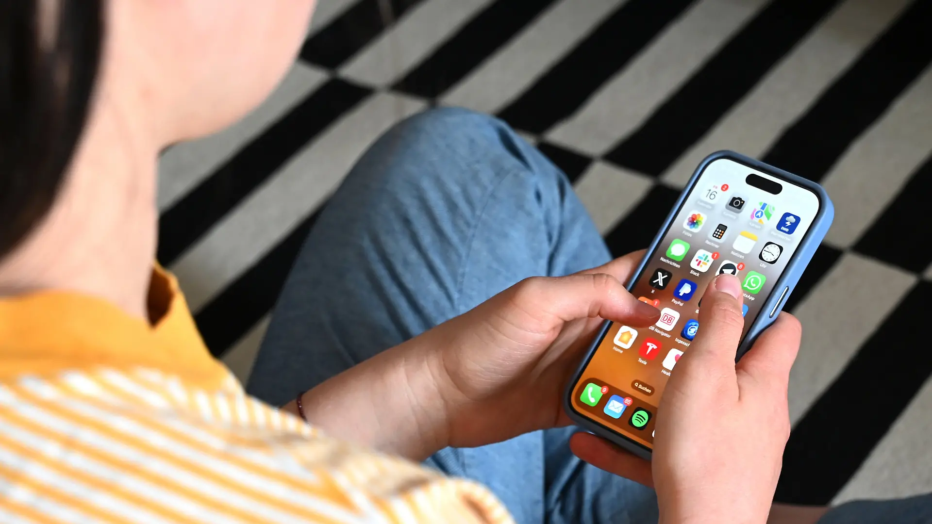SYMBOLBILD - 17.05.2025, Sachsen, Leipzig: Eine Jugendliche sitzt auf dem Boden und nutzt ein Smartphone - auf dem Display sind verschiedene Apps zu sehen. (zu dpa: «Social-Media-Verbot: Könnte ein EU-Bericht den Weg ebnen?») Foto: Elisa Schu/dpa +++ dpa-Bildfunk +++